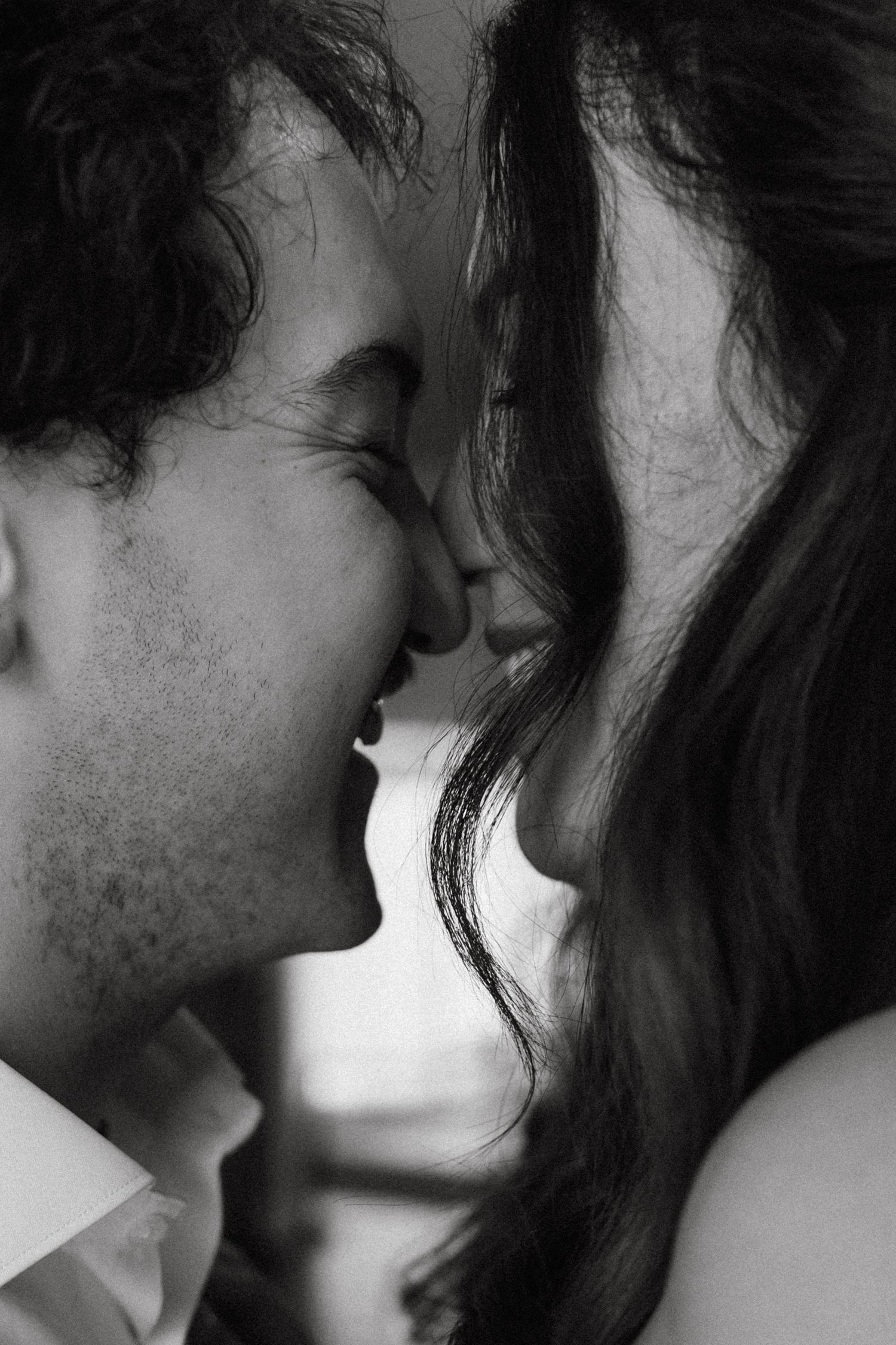 Black and white close-up of a couple sharing an intimate moment, noses touching and smiling.