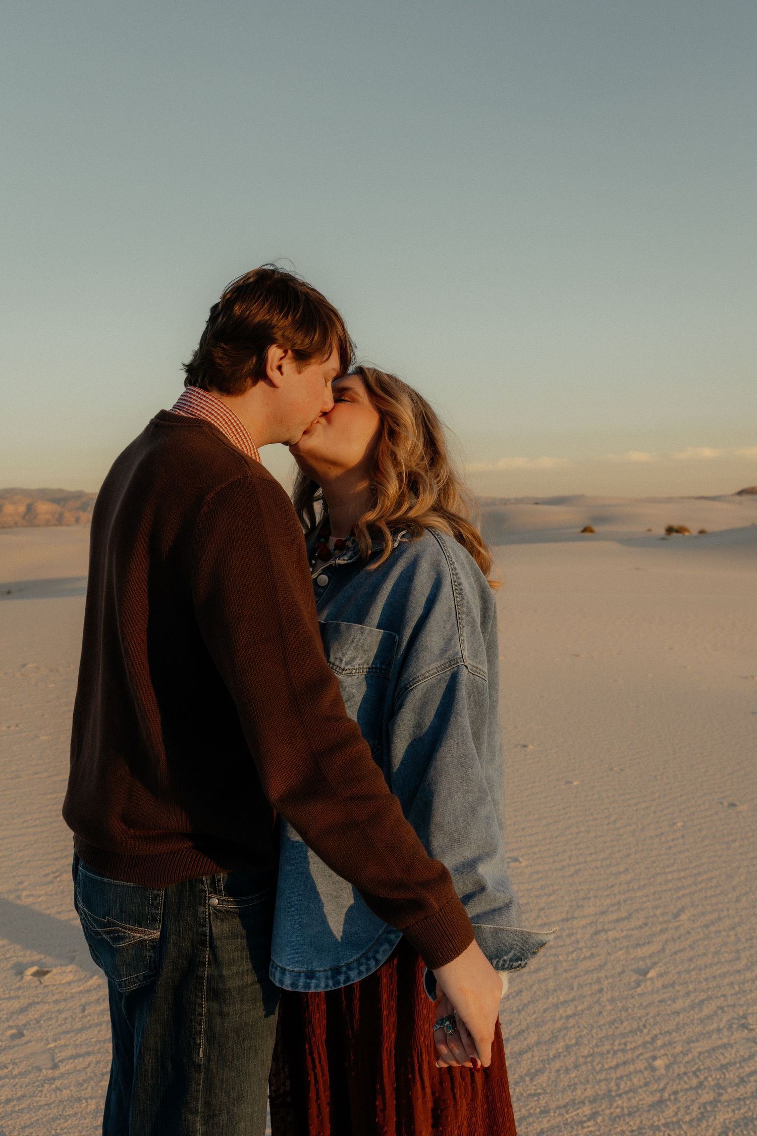 Couple kissing on white sand dunes at sunset in the desert.