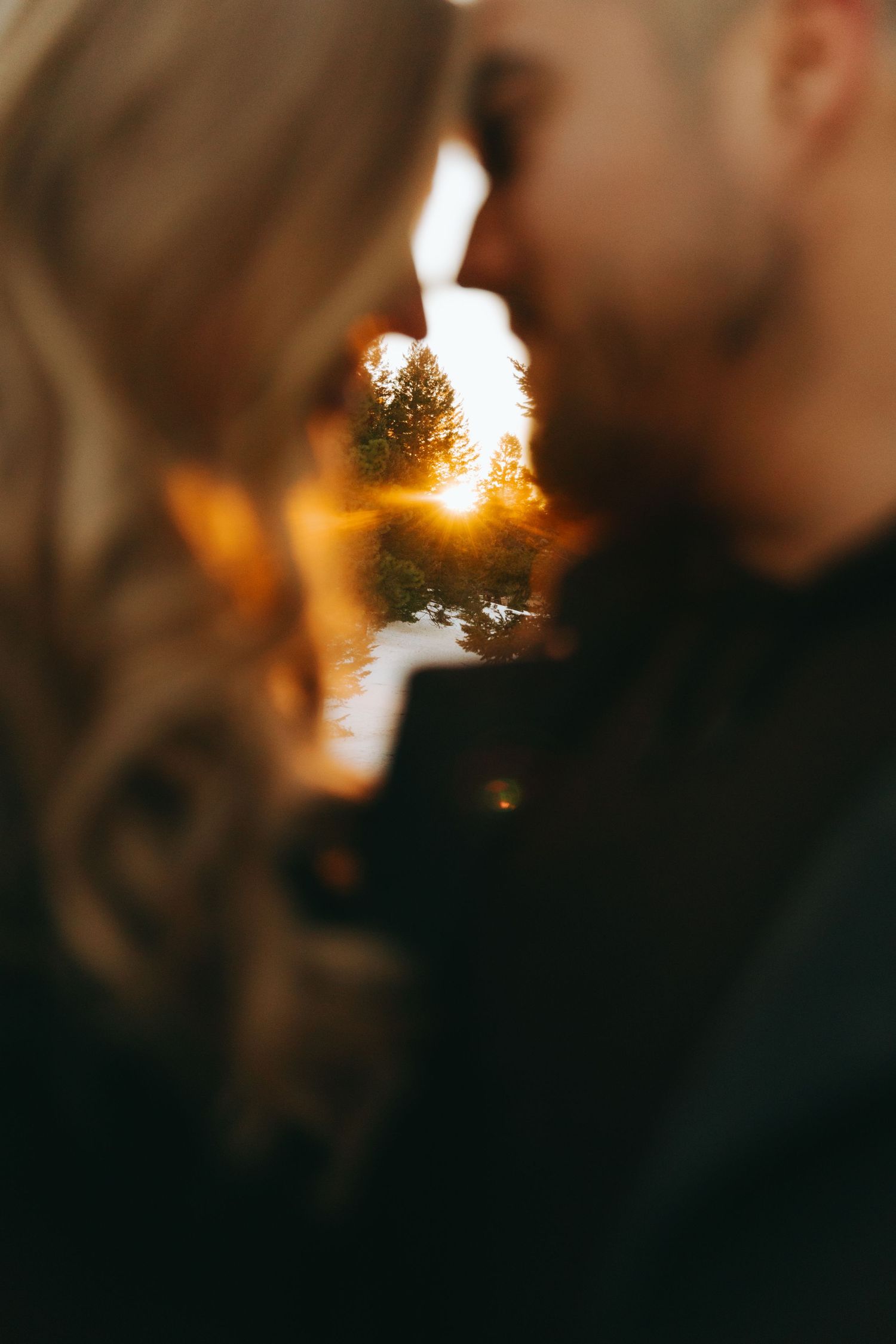 A couple shares a romantic moment at golden sunset, framed by warm bokeh light between their faces.