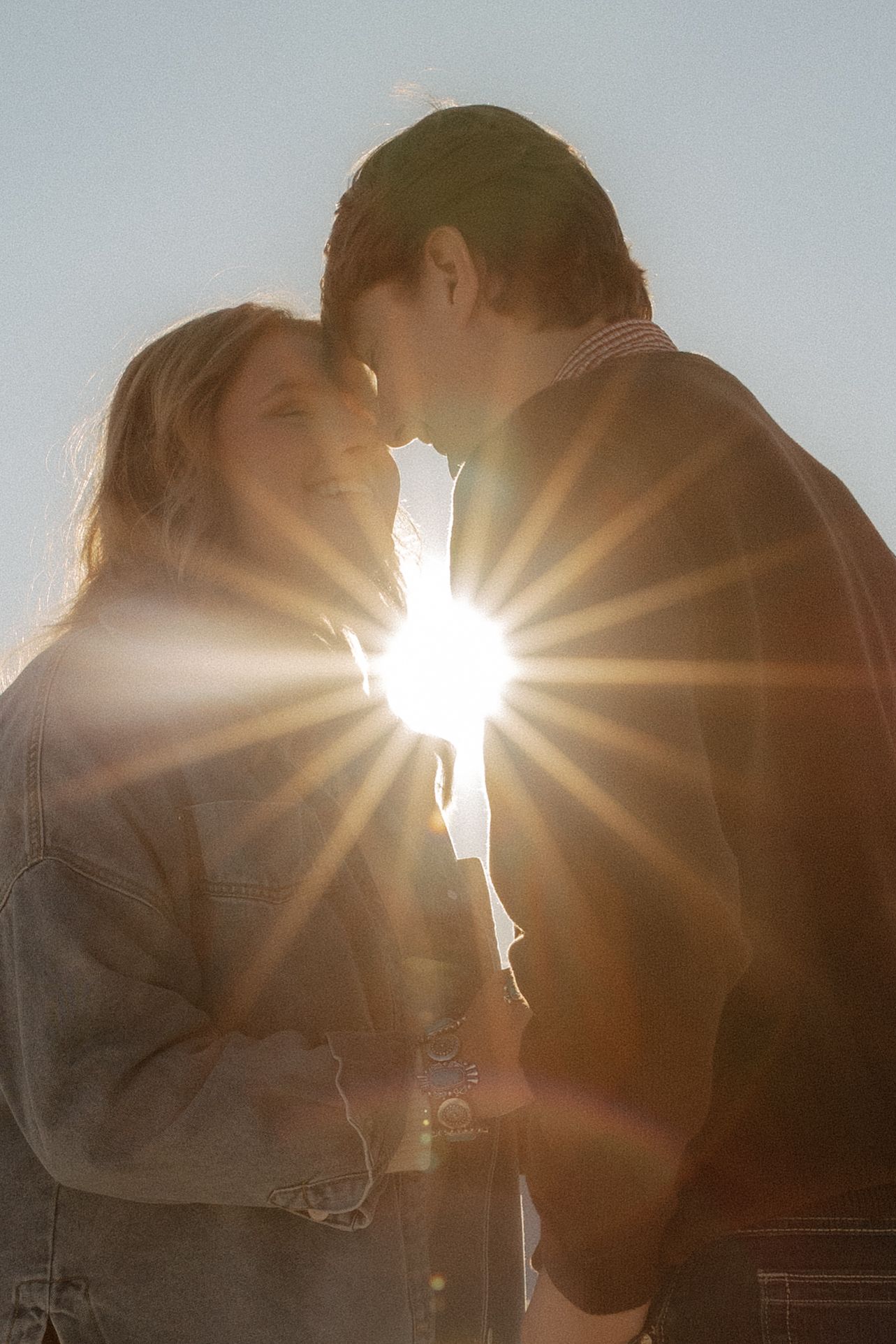 Romantic couple sharing an intimate moment backlit by a stunning sunburst flare against a bright sky.