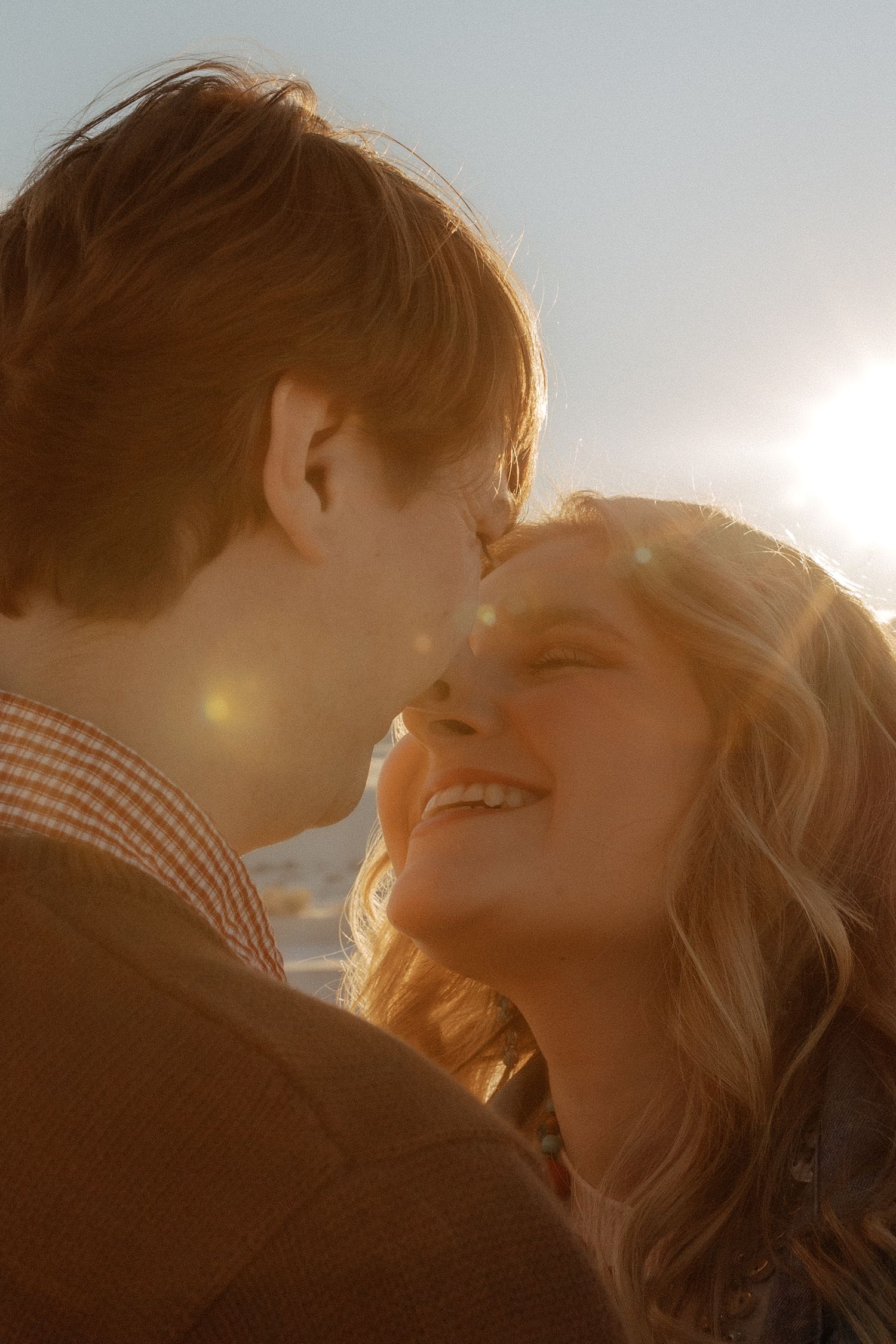 Happy couple sharing a tender moment outdoors, bathed in warm golden sunlight with a bright lens flare.