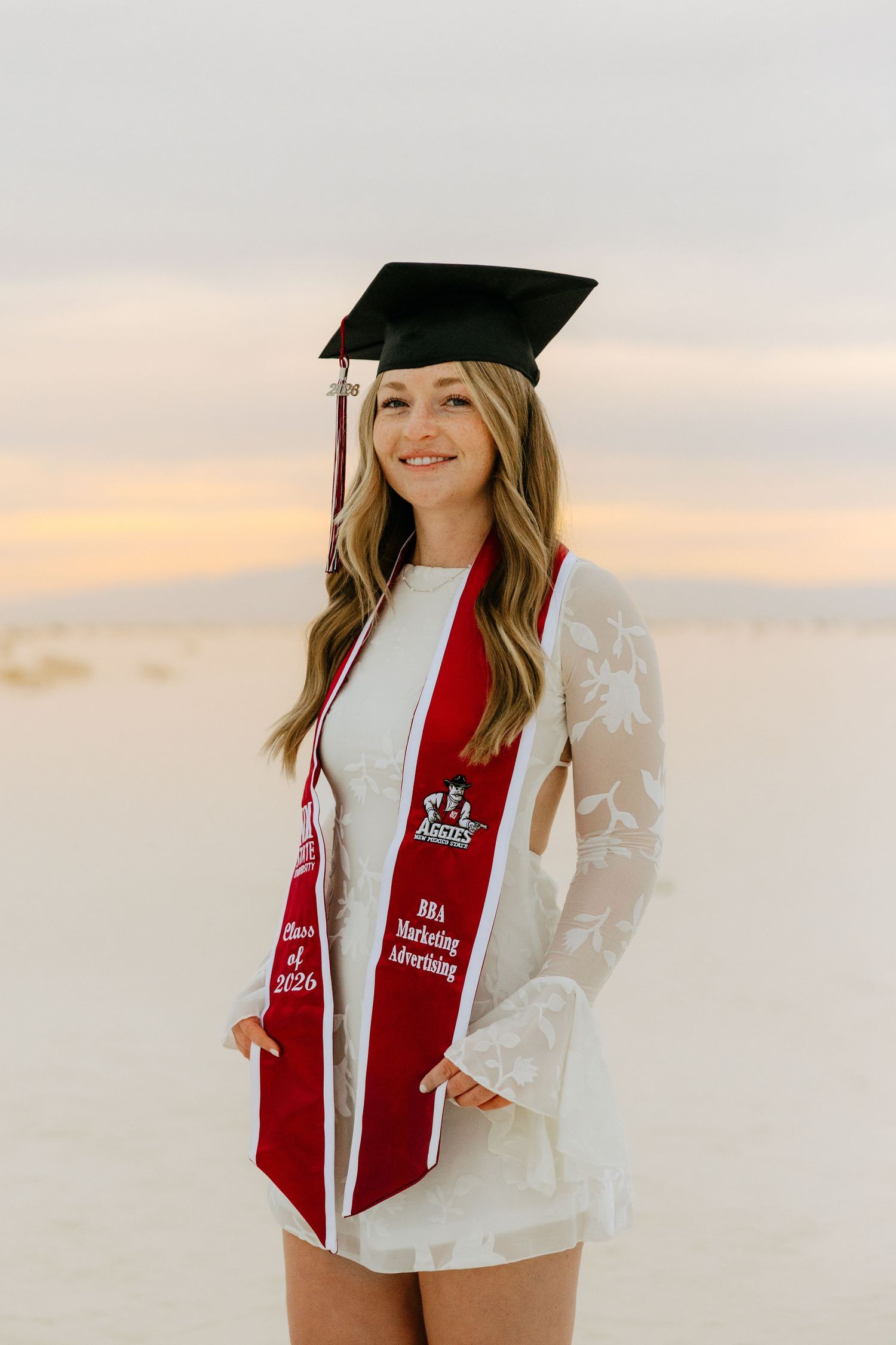 Graduate smiling in white lace dress with red BBA Marketing Advertising stole and cap.
