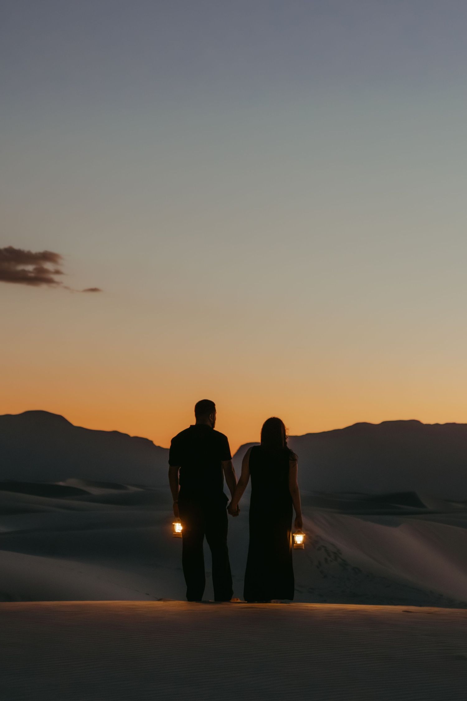 Couple holding lanterns hand in hand silhouetted against a stunning desert sunset at White Sands.