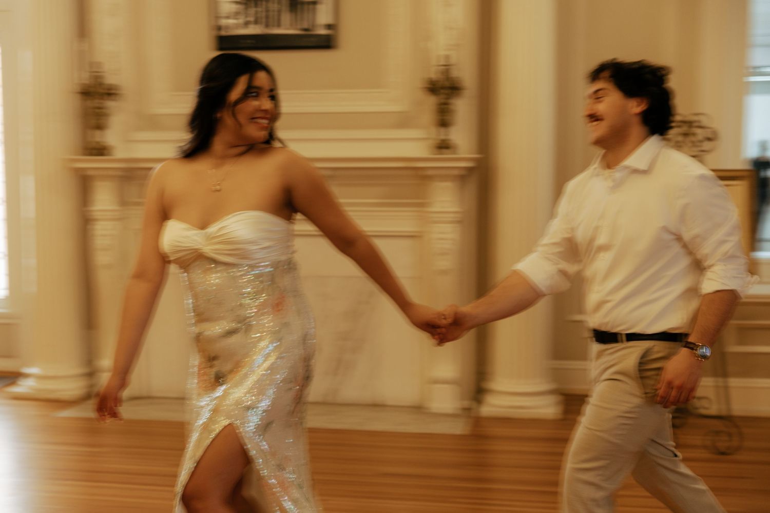 Couple dancing joyfully hand in hand at elegant indoor wedding reception.