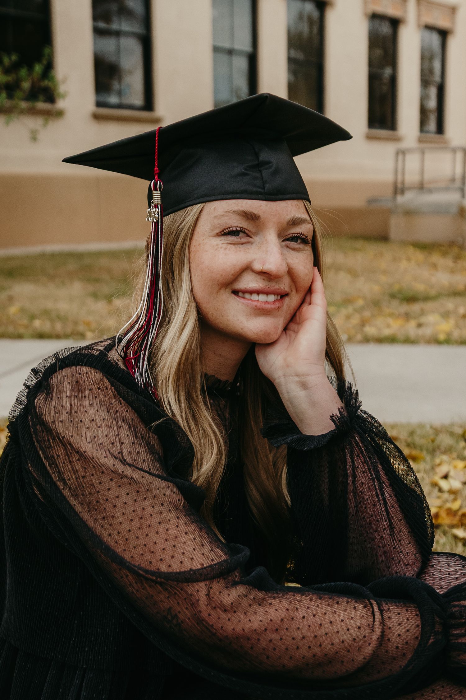 Smiling graduate in black cap and sheer dress posing for graduation photos outdoors.
