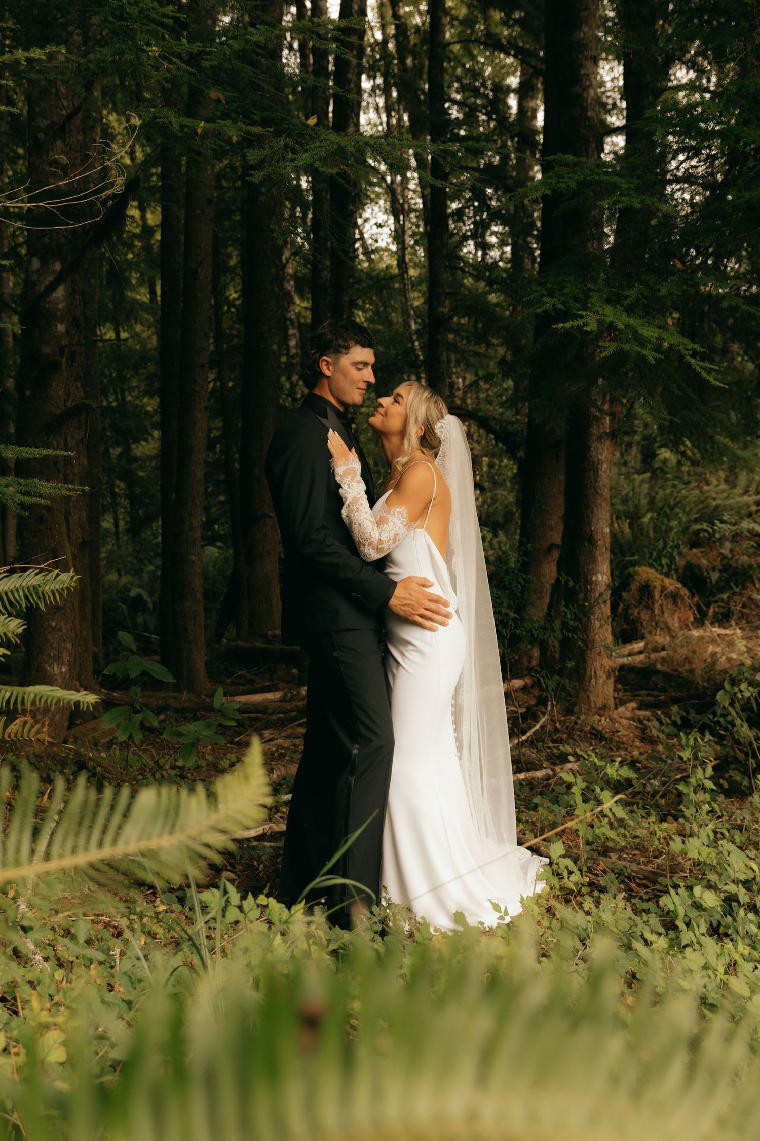 Bride and groom sharing a romantic kiss in a lush forest setting, bride wearing a white gown with veil.