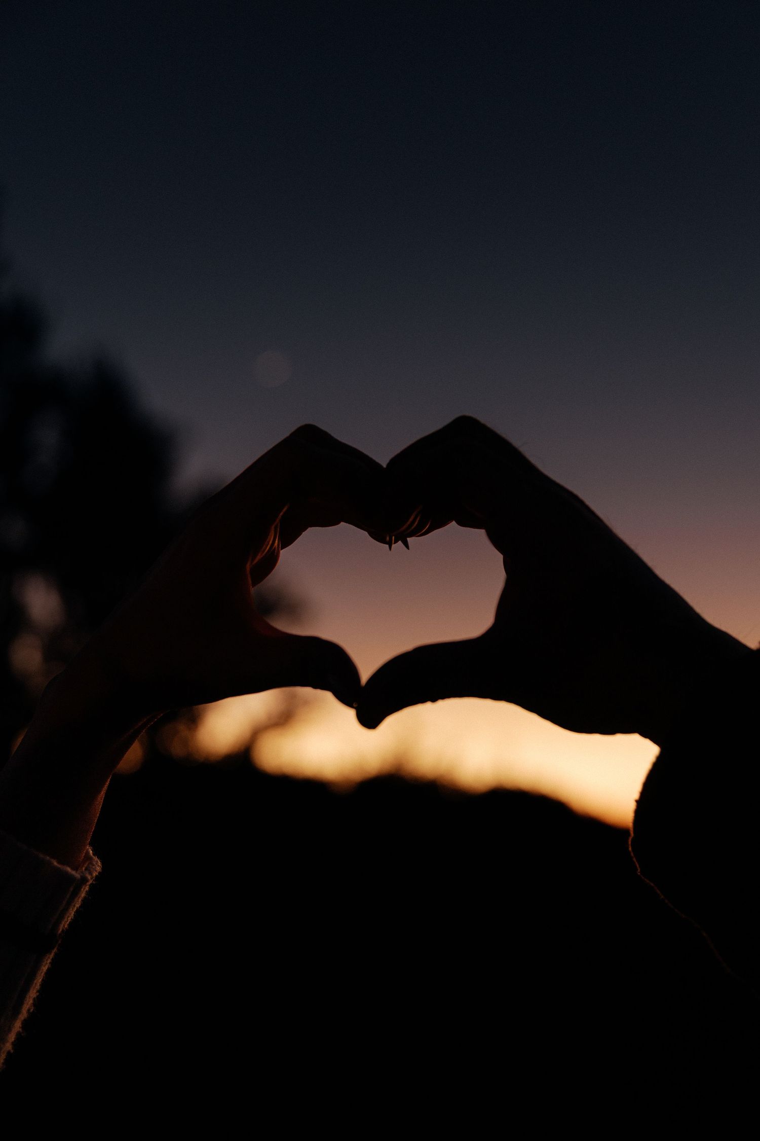 Silhouette of two hands forming a heart shape against a warm golden sunset sky.