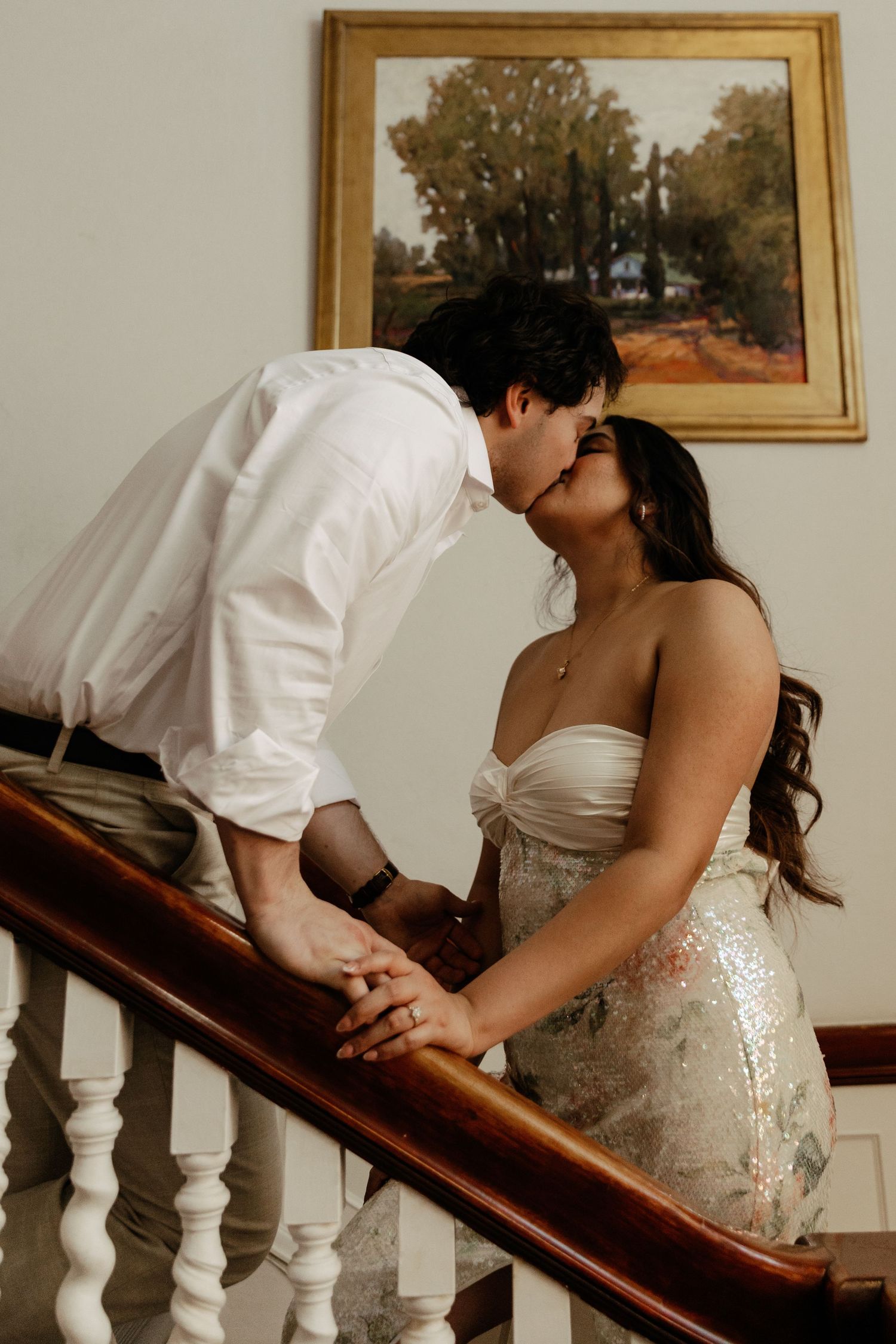 Romantic couple kissing on a staircase, man in white shirt and woman in sparkly dress.