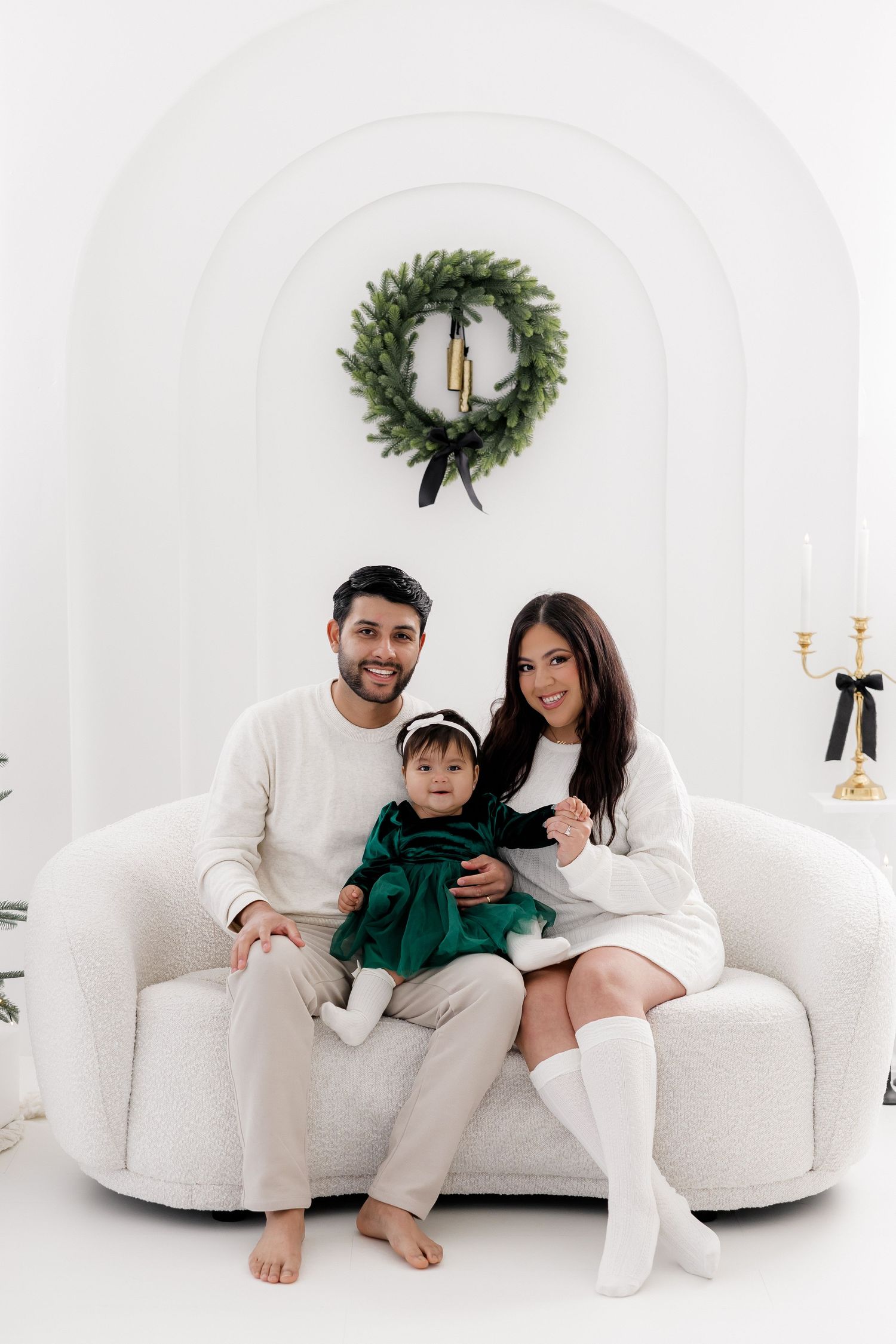 Family relaxing together on white couch with Christmas decorations in background.