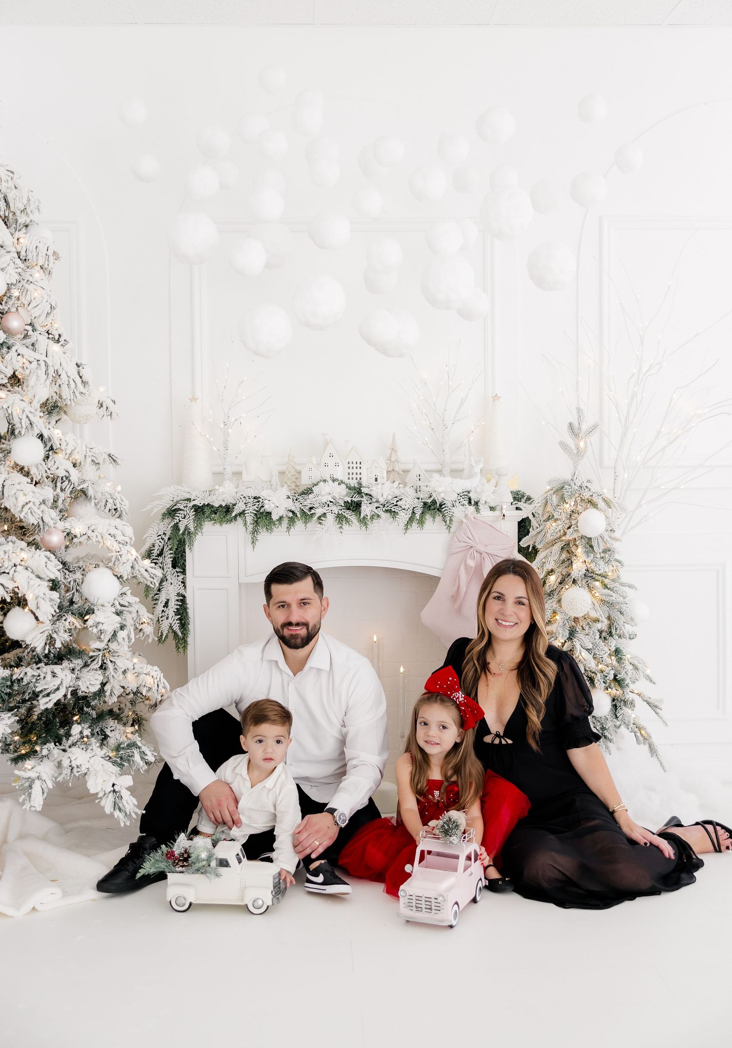 A family of five poses in coordinated holiday outfits against a winter white Christmas backdrop.