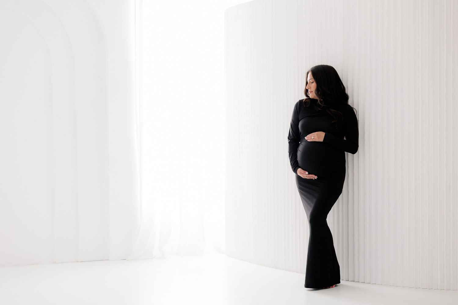 A series of black and white photos showing a pregnant woman in a black dress posing against a white wall.
