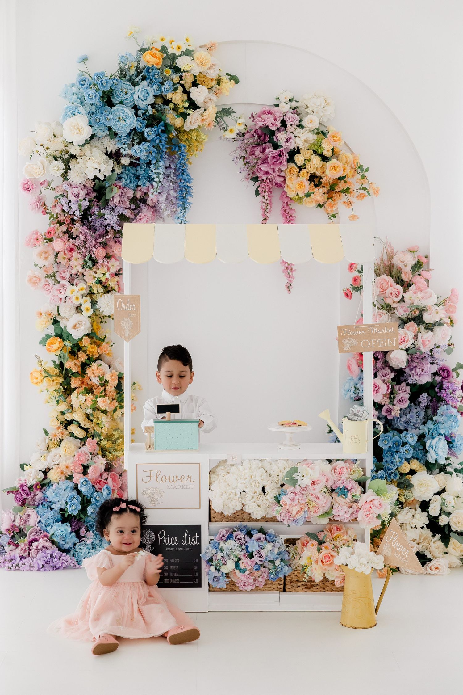 Colorful floral backdrop setup with pink, blue, and yellow flowers arranged around white frames for photo sessions.