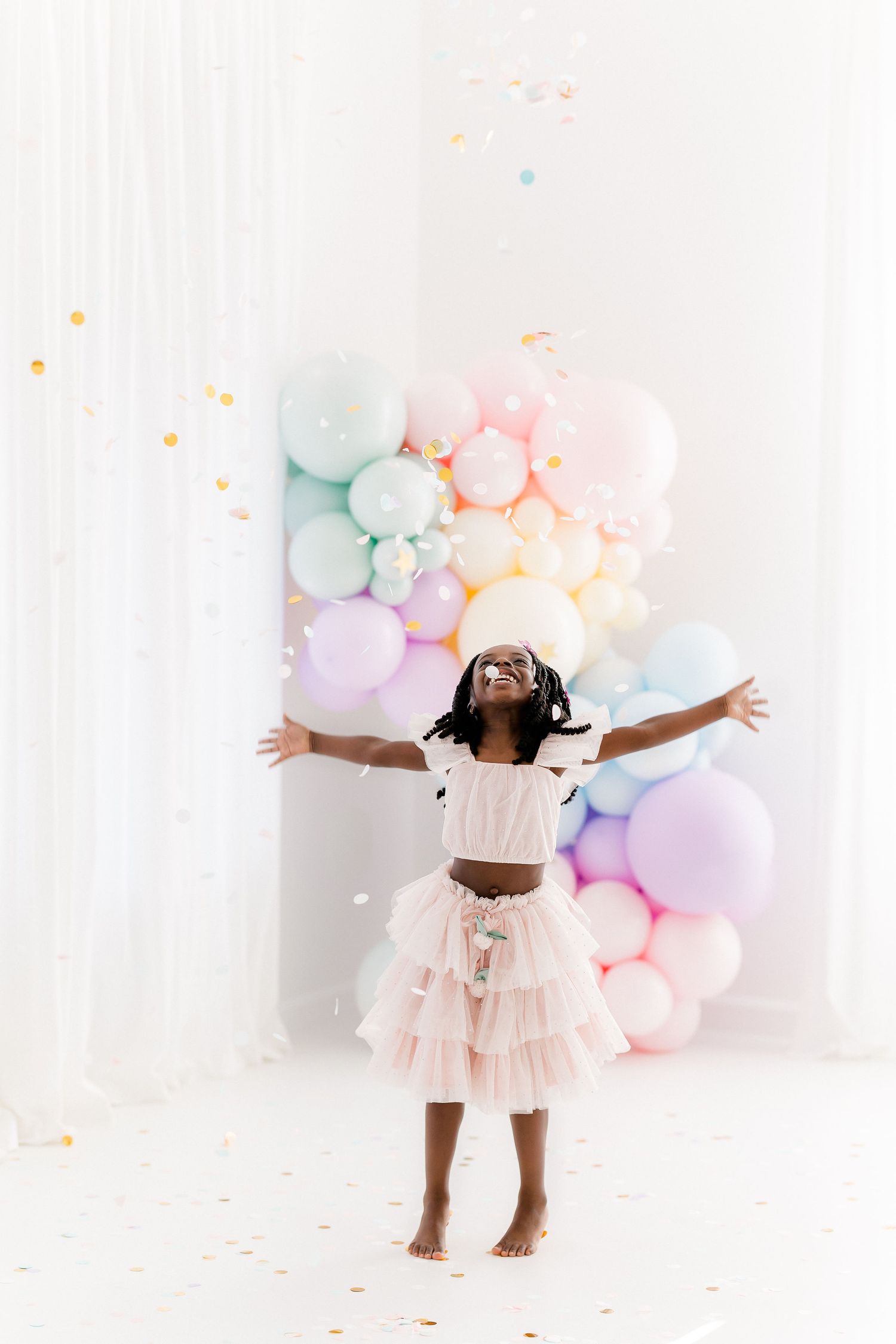 A whimsical scene with pastel balloons and confetti featuring someone in a pink tulle skirt dancing joyfully.