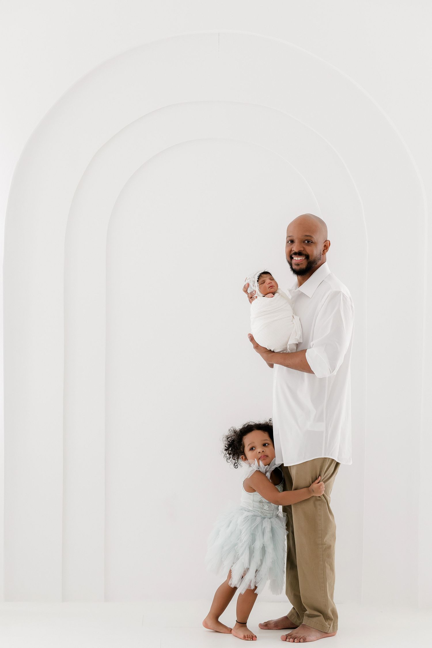 Heartwarming family portrait in white outfits against minimalist white studio backdrop.