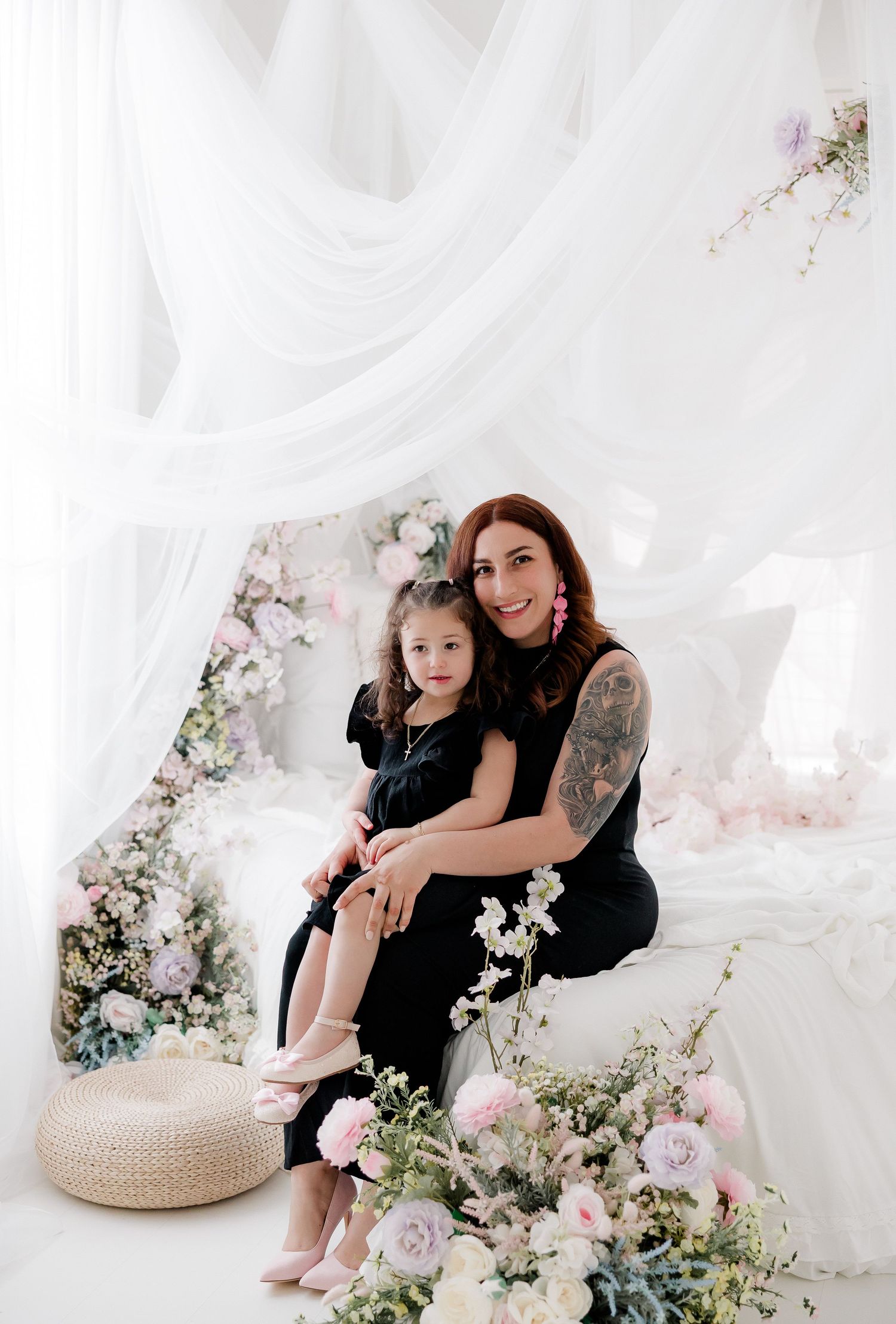 A dreamy white studio setting decorated with delicate floral arrangements and draped fabric creates an ethereal atmosphere.