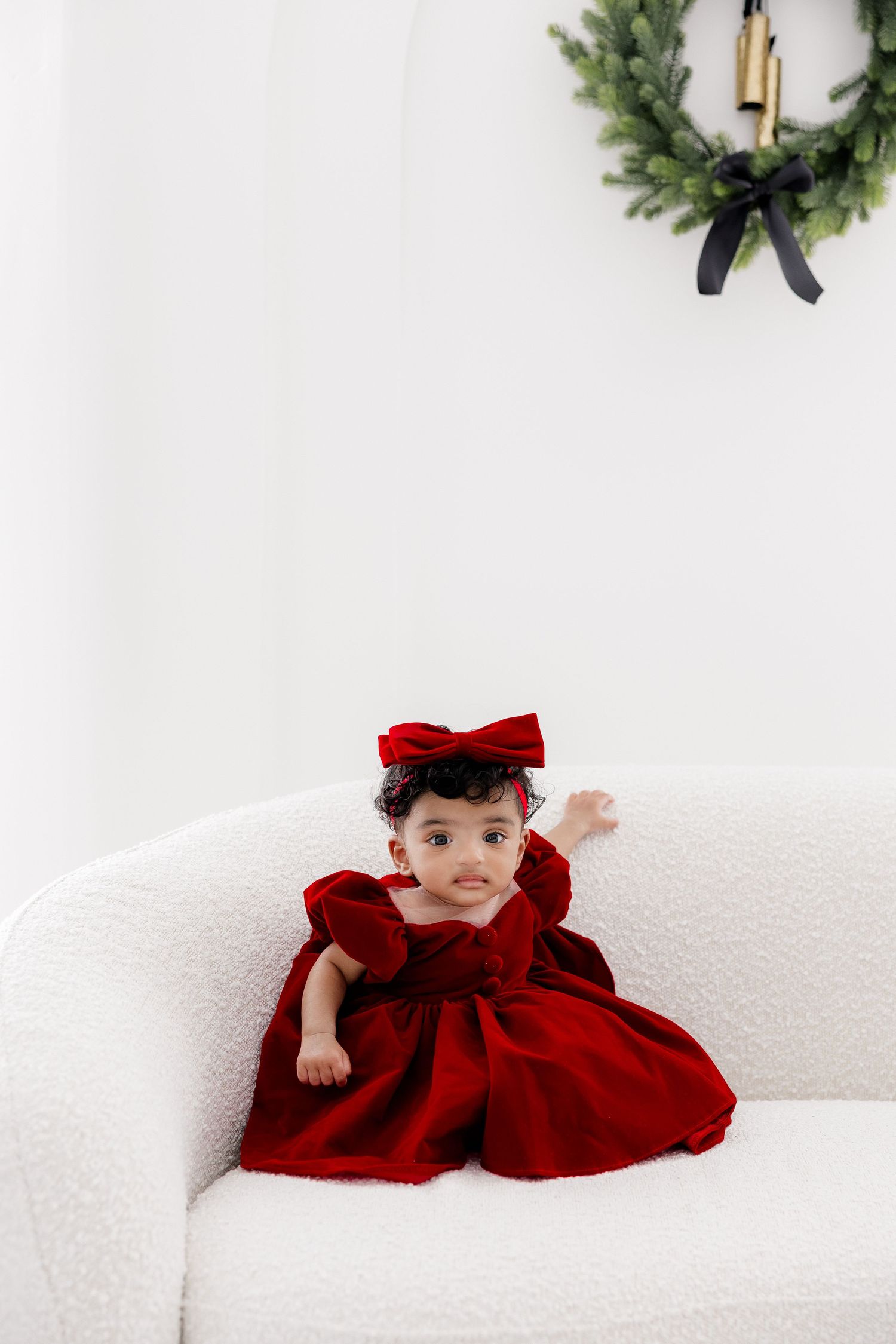 A red velvet dress lies draped across a white sofa in a minimalist holiday setting.