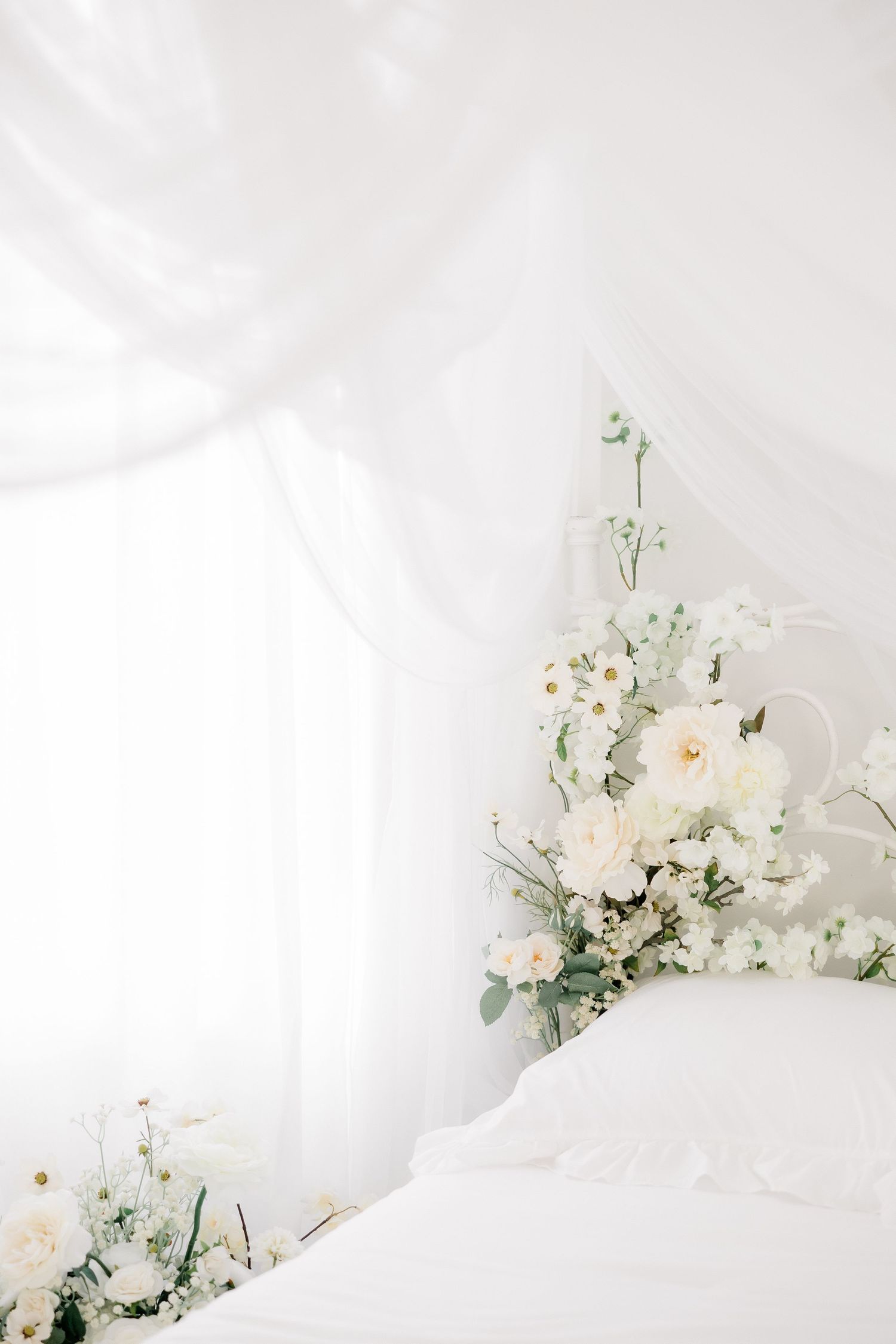 Delicate white floral arrangement with blush accents against soft white linens and airy fabric backdrop.