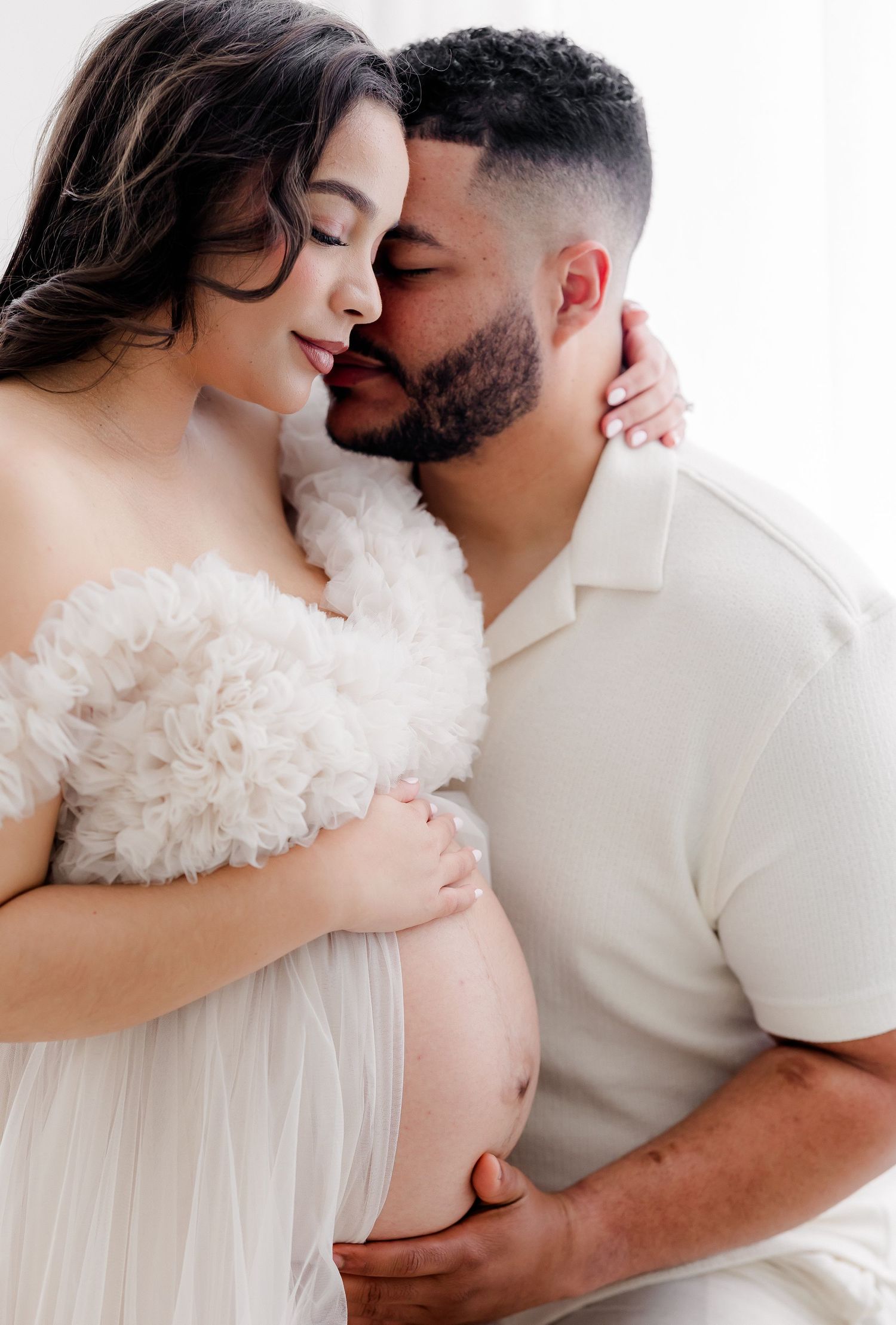 Intimate couples maternity portrait in white with soft romantic styling and natural poses.