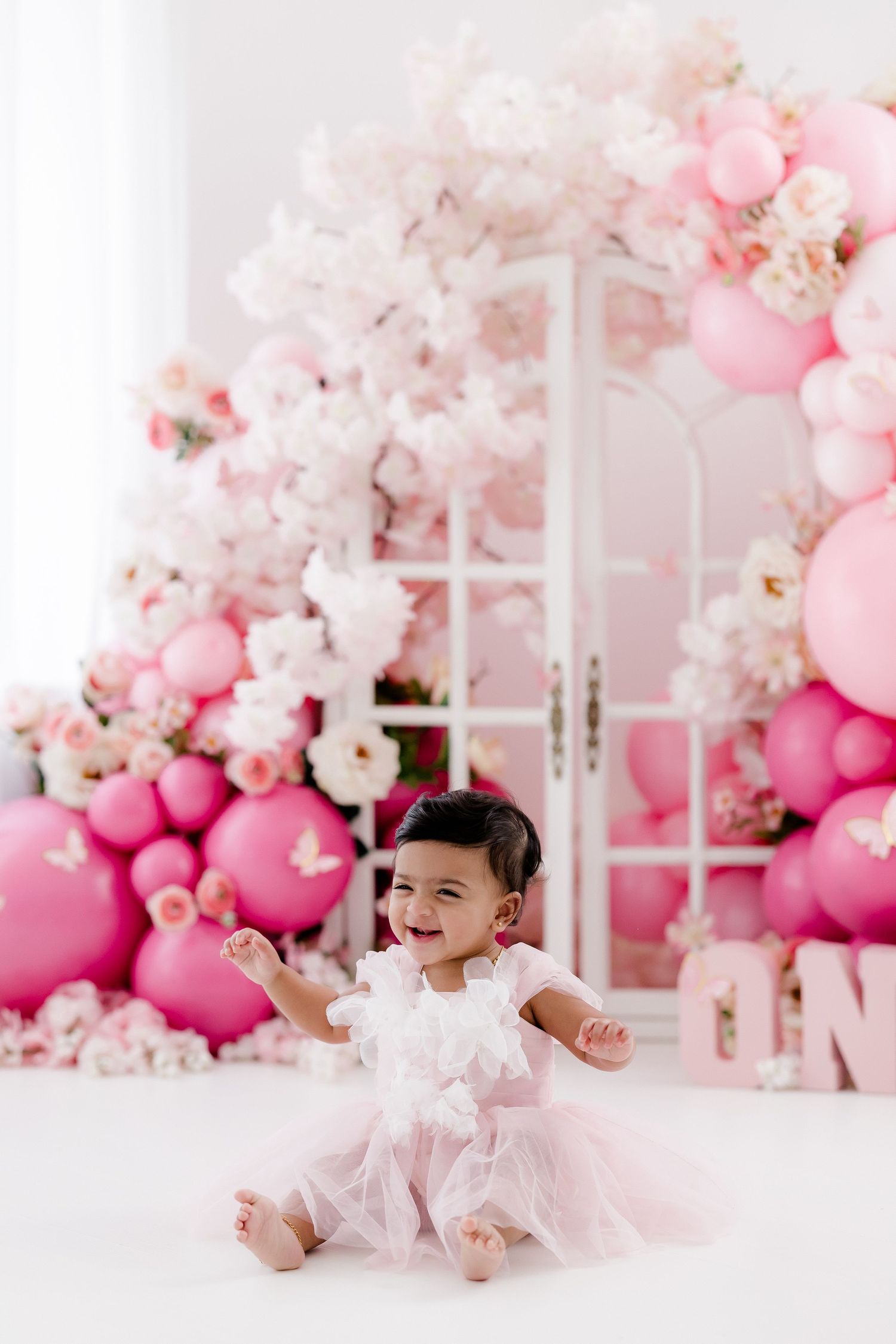 Pink balloon garland and floral decorations create a romantic backdrop in a bright white studio.