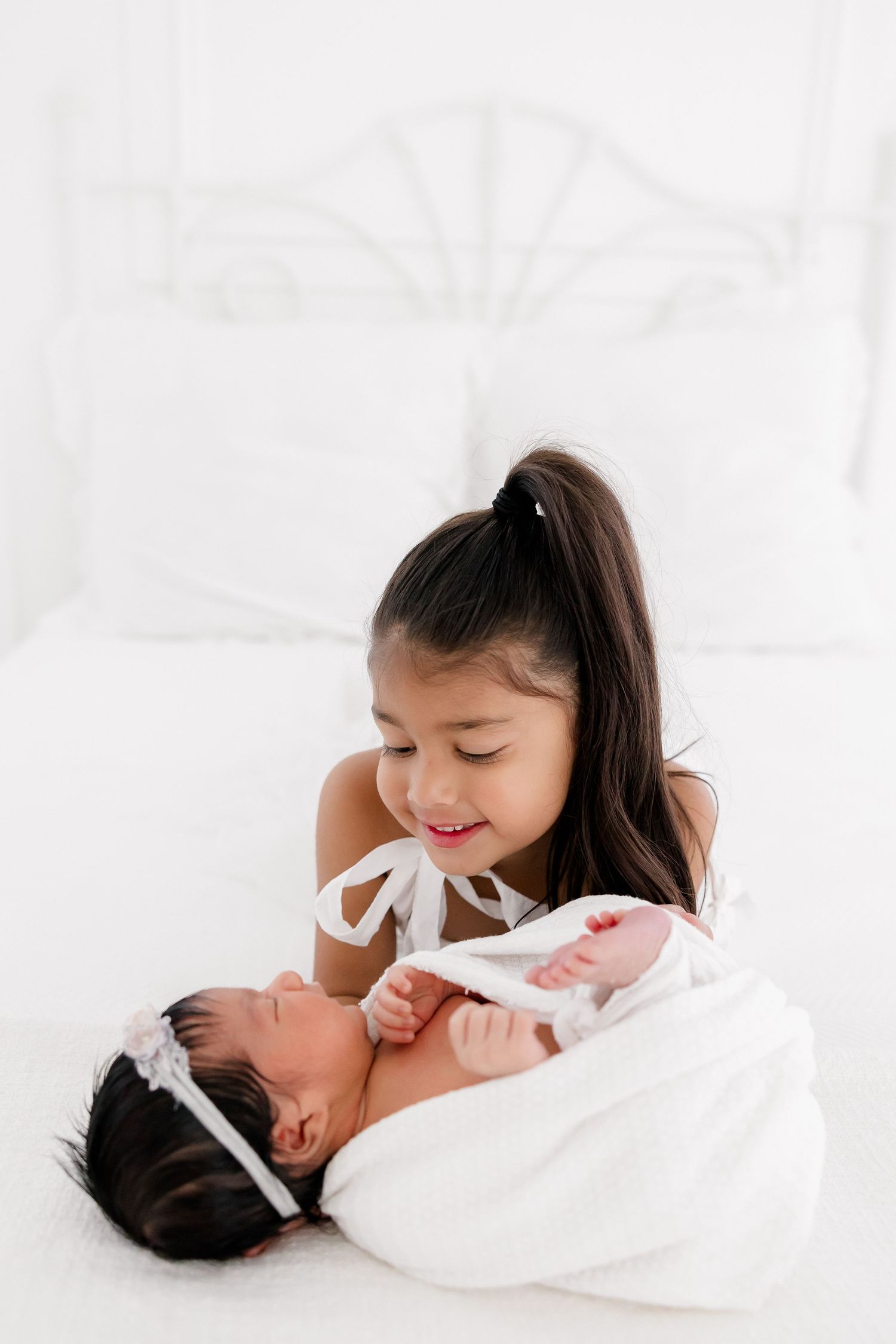 Siblings share sweet moment with newborn baby on white background.