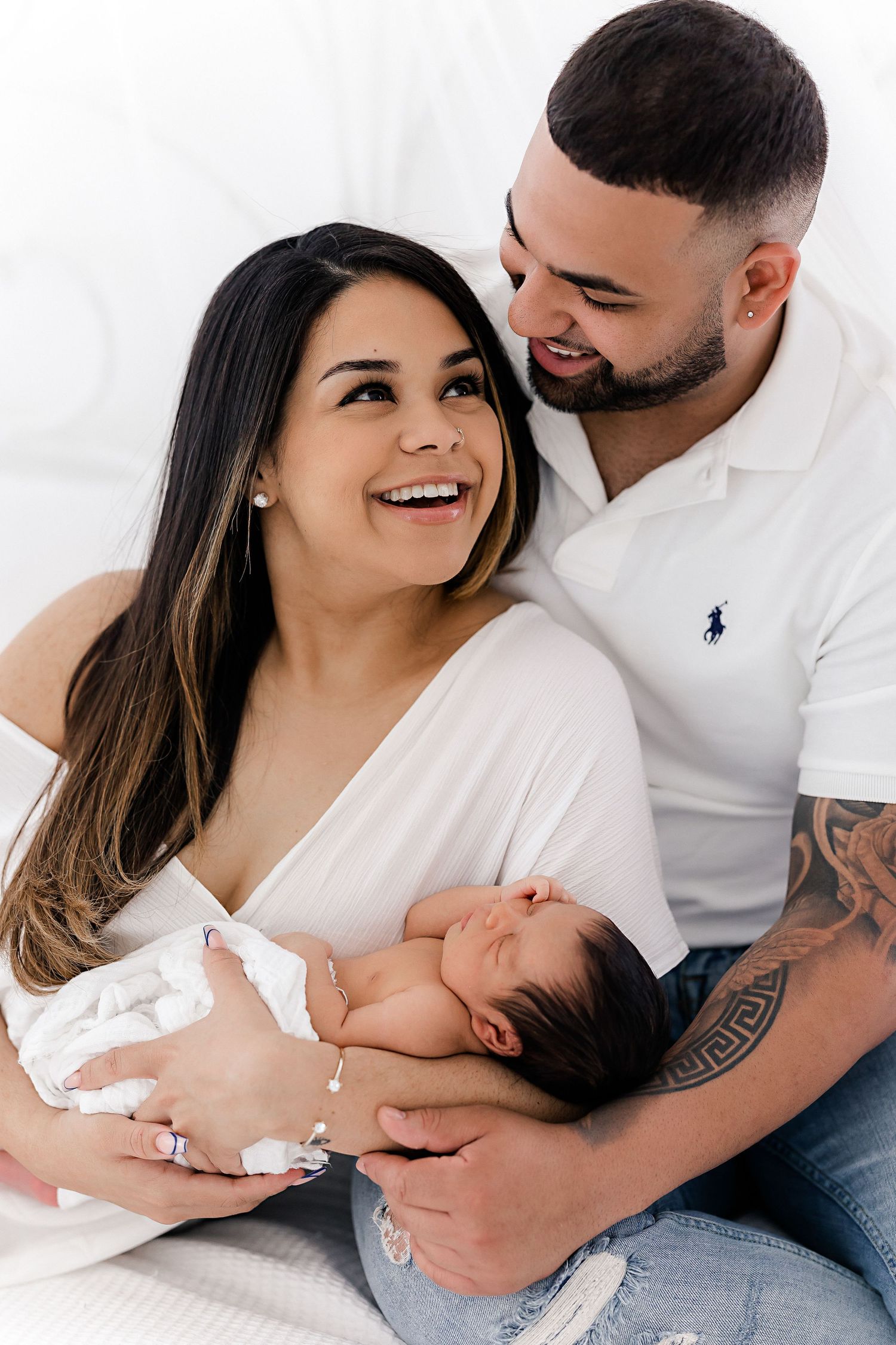 Parents in white clothing share tender moments with their newborn baby.