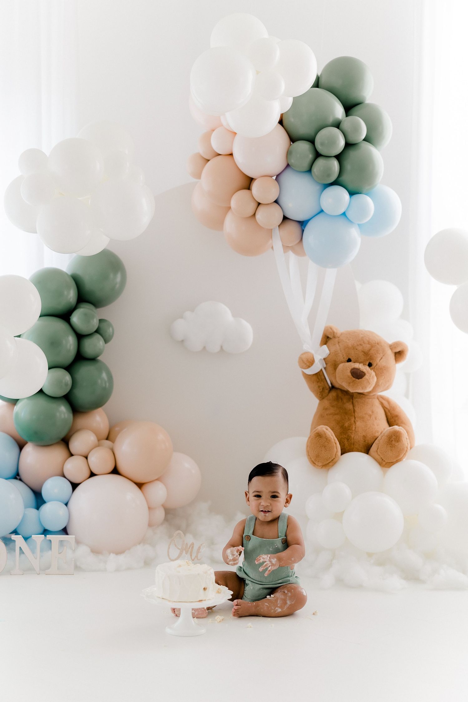 Pastel balloon arch with teddy bear creates sweet baby photography backdrop.