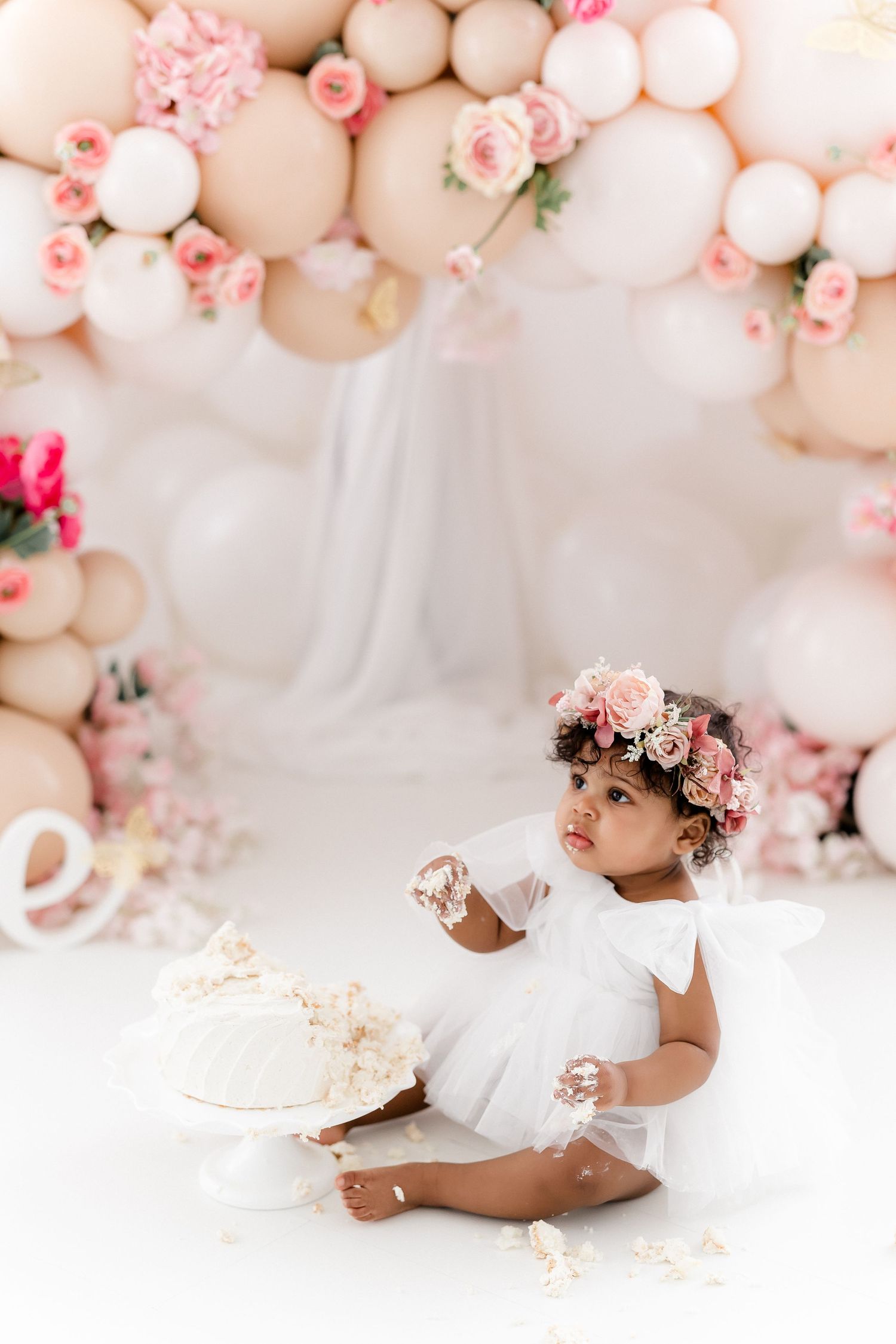 Cake smash photography session with pink balloon arch and floral decorations.