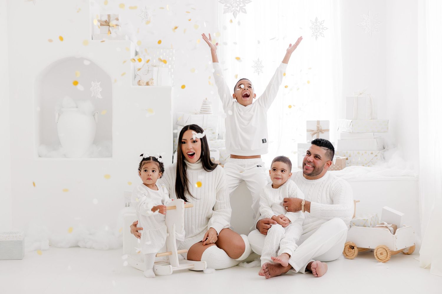 Family group in white outfits celebrating with gold confetti in bright studio setting.nj holiday mini sessions