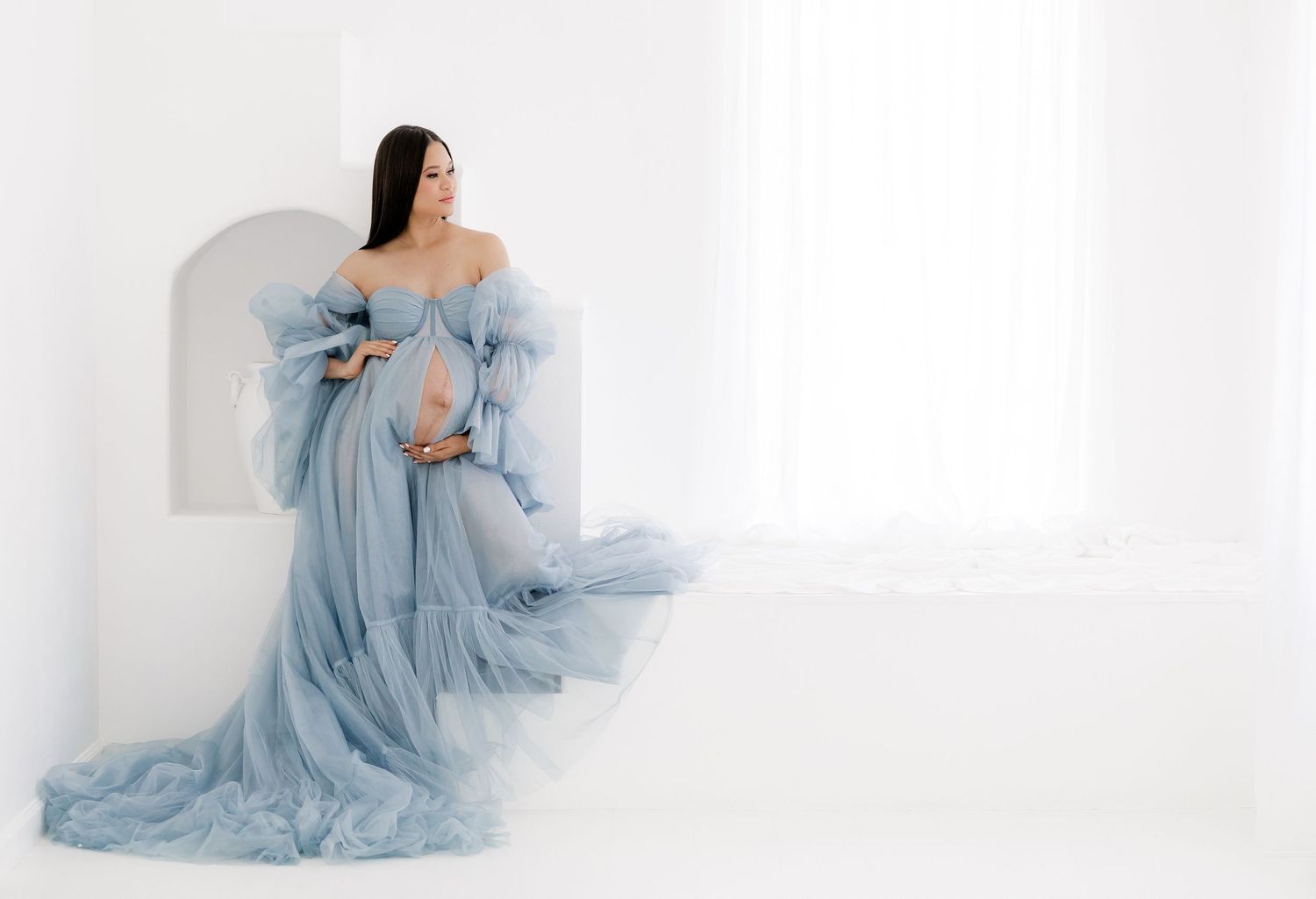A woman in an ethereal light blue flowing dress poses gracefully against a white backdrop.