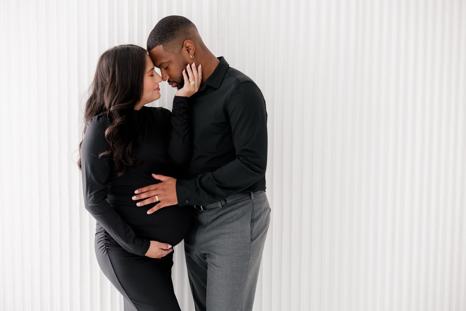 A couple in black attire sharing an intimate moment in front of a white backdrop.