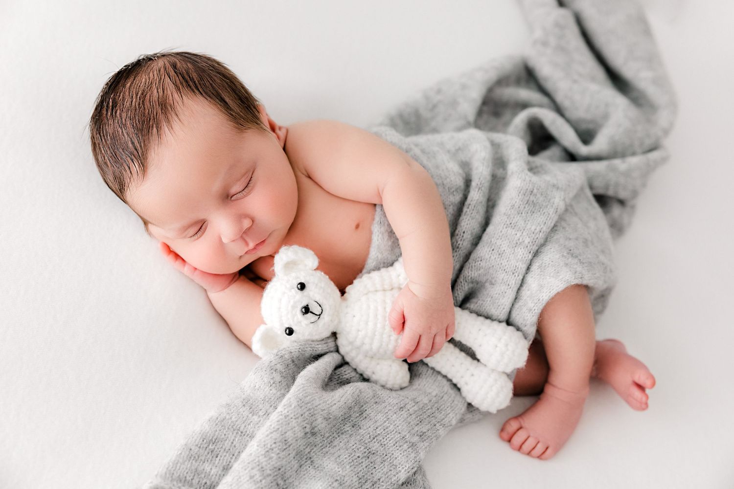 Sleeping newborn baby wrapped in soft gray blanket with white stuffed animal companion.