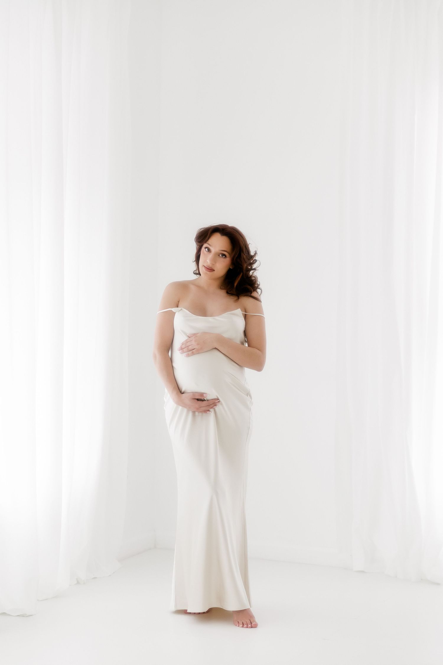 Elegant maternity portrait series in white dress against bright studio backdrop showing different graceful poses.