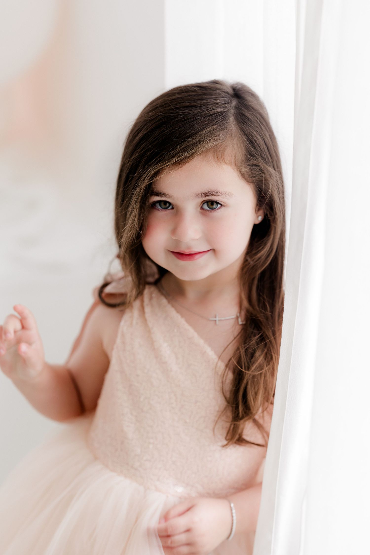 A young girl in a soft peach dress smiles sweetly in a series of four connected portrait photographs.