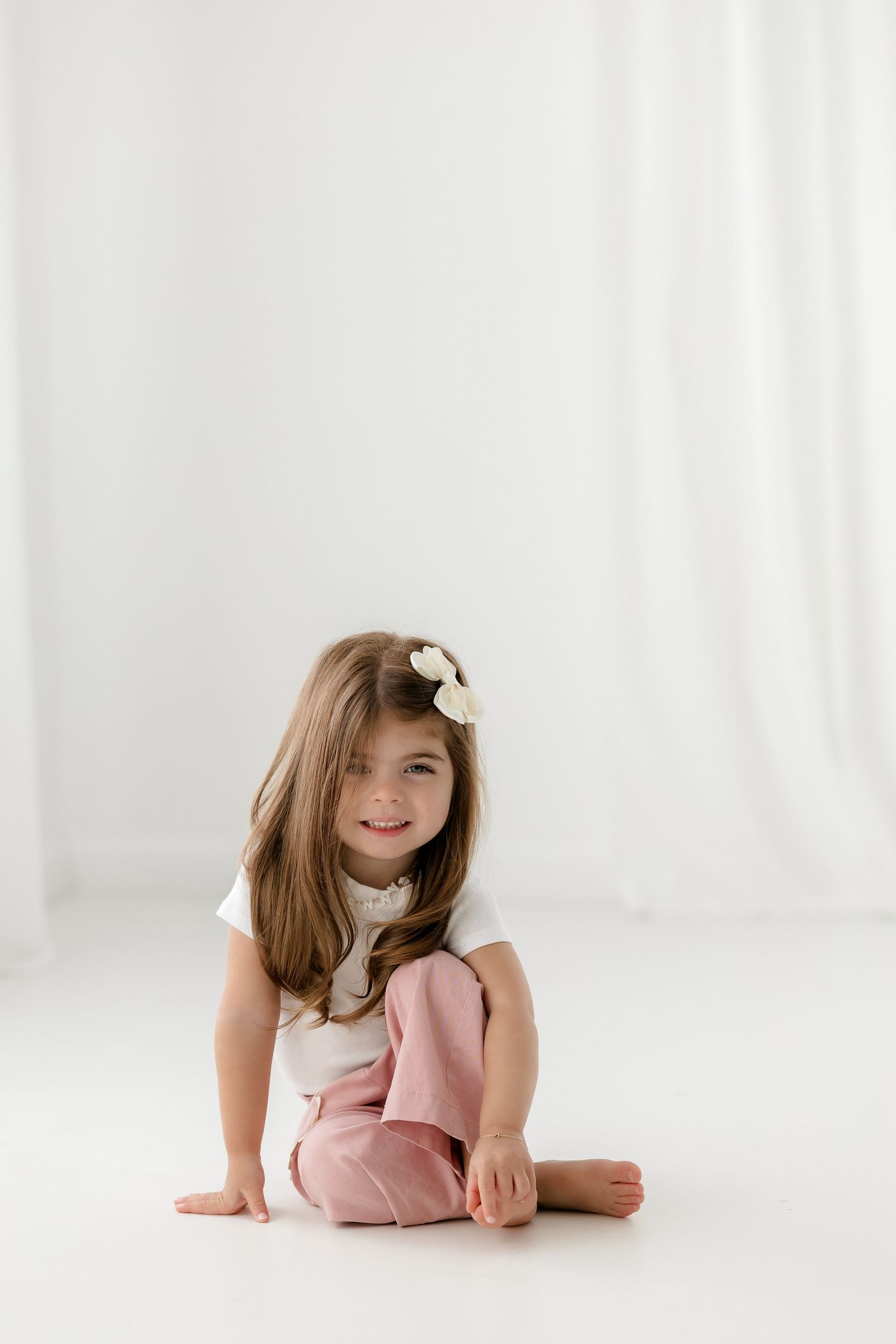 Young child in pink dress lying on white floor with soft natural lighting.