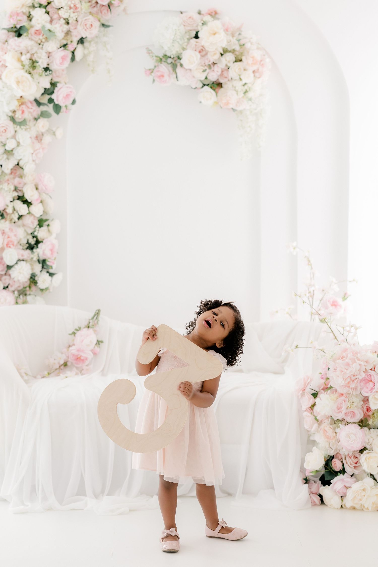A child in a pink dress dances in a dreamy white room decorated with pink and white floral arrangements.
