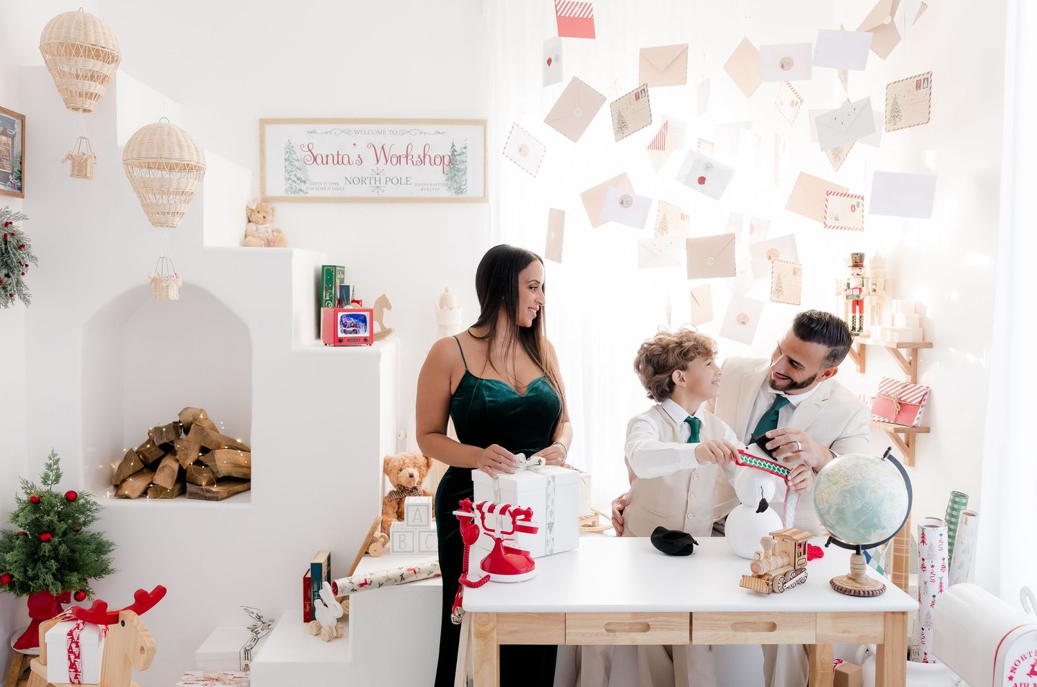 Family posing in a festive Santa's workshop Christmas mini session with white walls and holiday decorations.