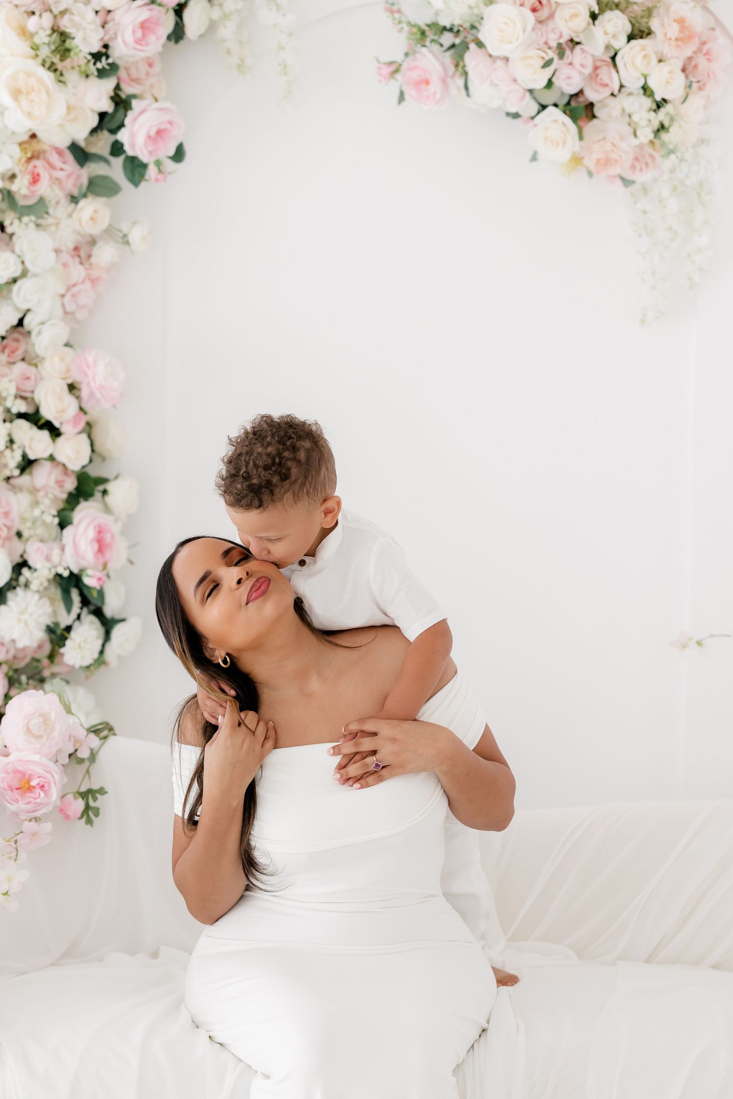 A romantic moment against a white wall decorated with pink and white floral arrangements.