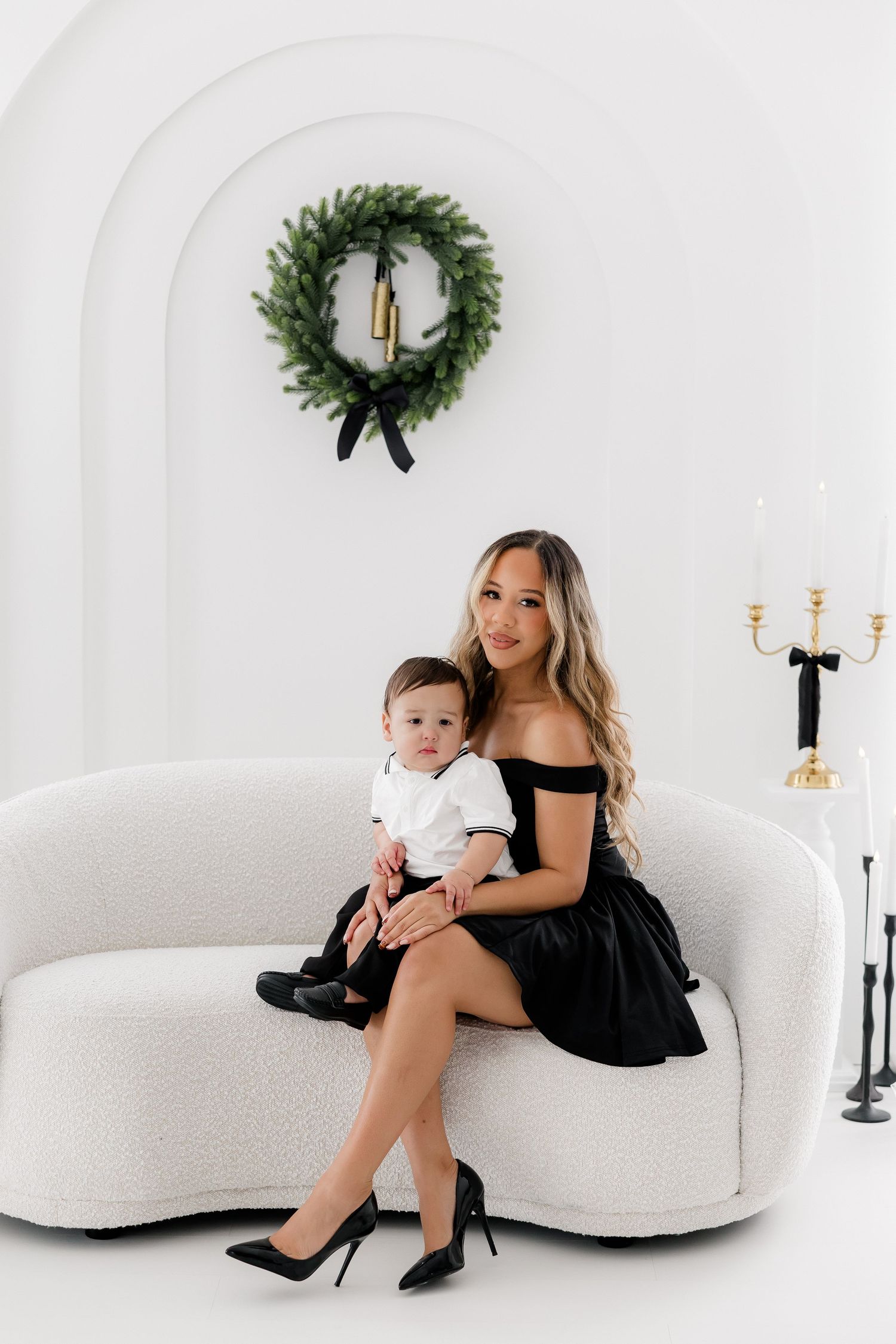 Elegant holiday portrait on white curved sofa with Christmas wreath and candles in background.