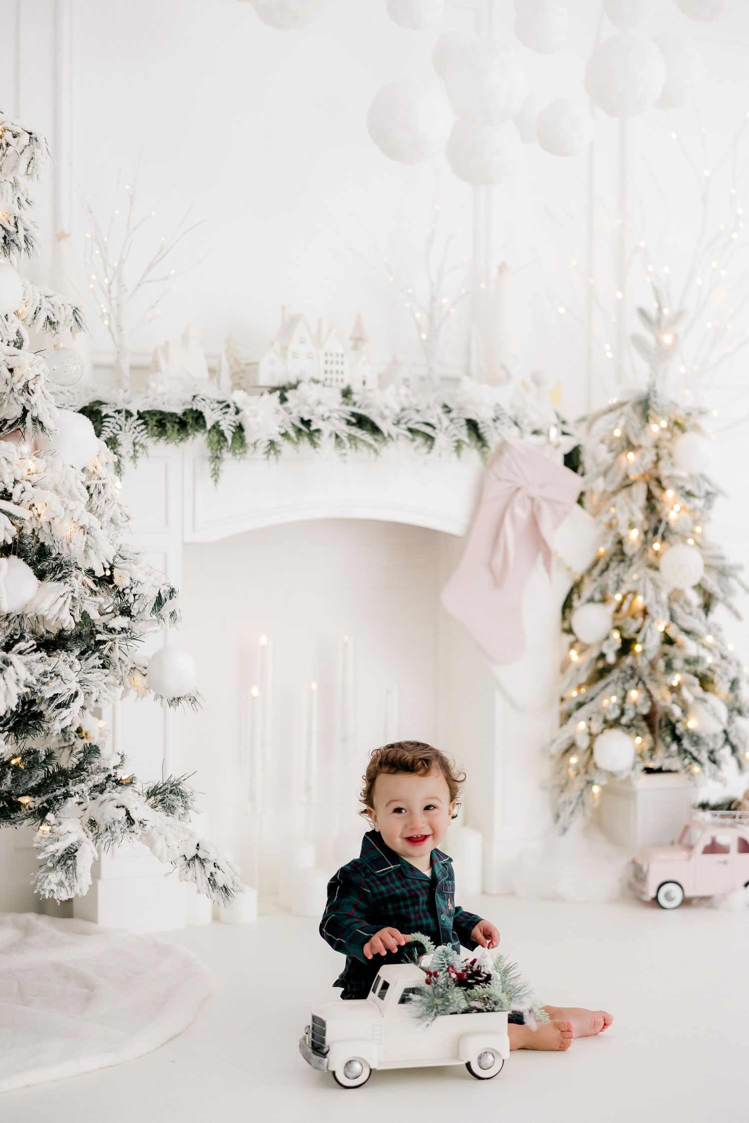 Child playing with vintage toy car in white winter studio setting with flocked Christmas trees.