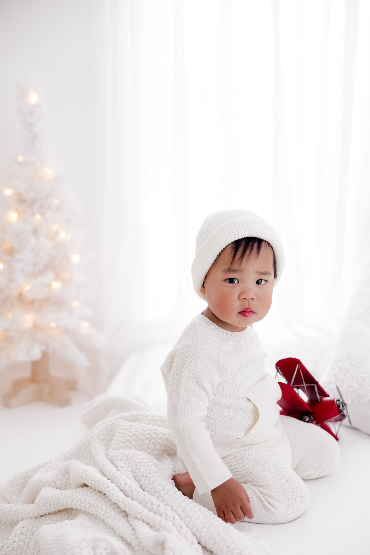 Winter themed baby photography with white blanket and soft Christmas lighting.