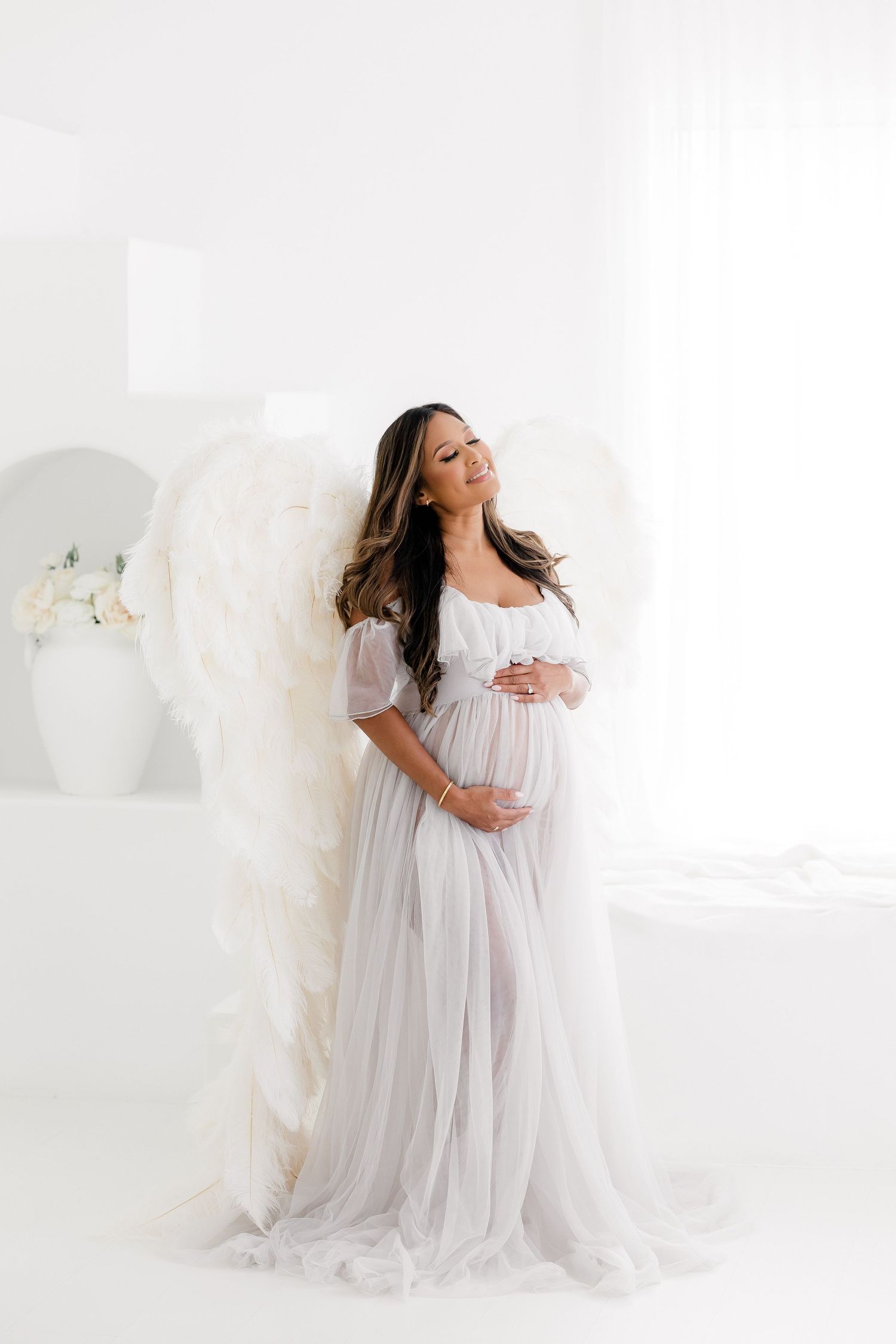 Ethereal maternity portraits in flowing white gown against bright studio backdrop.