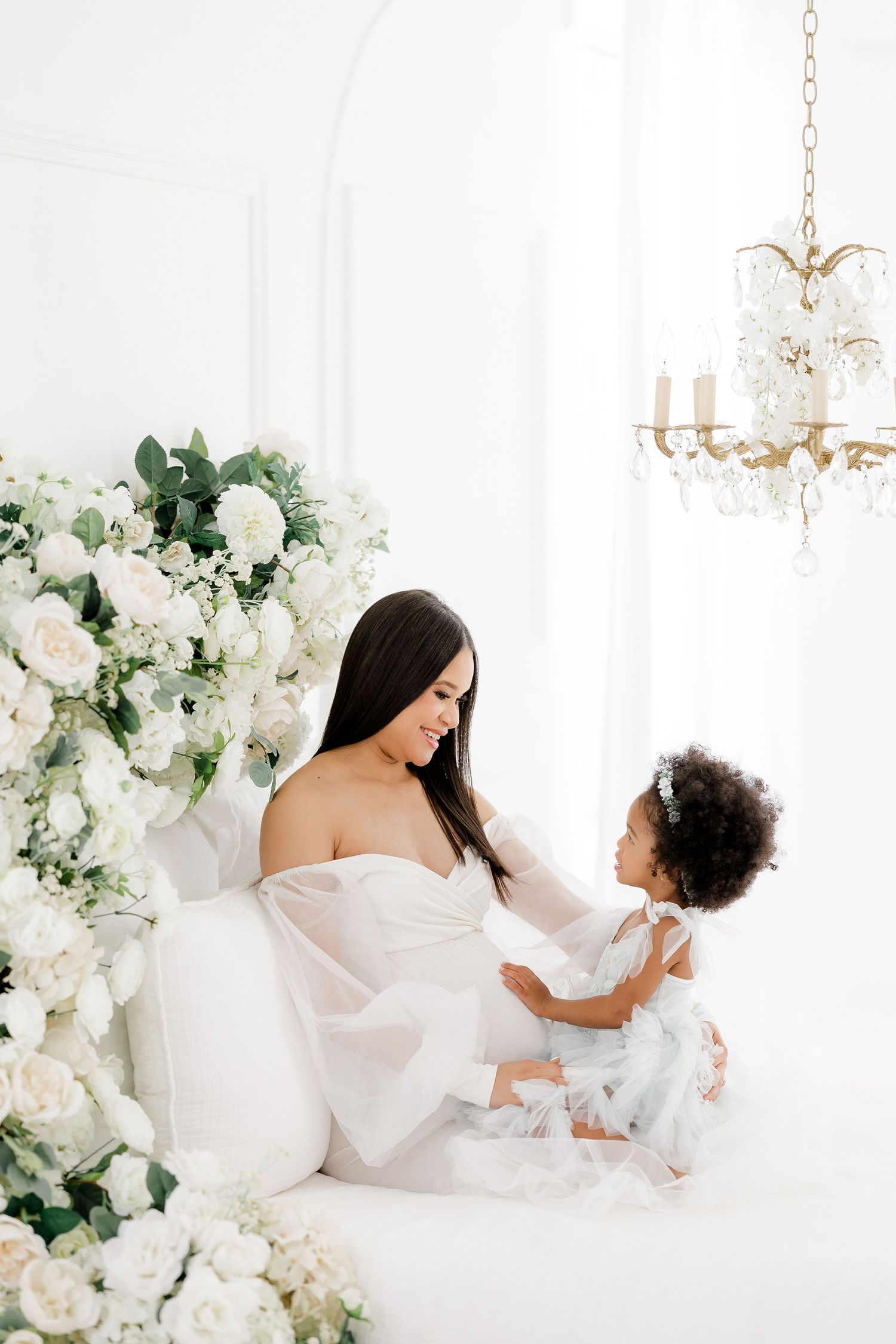 Elegant maternity session with white floral arrangements and crystal chandelier.