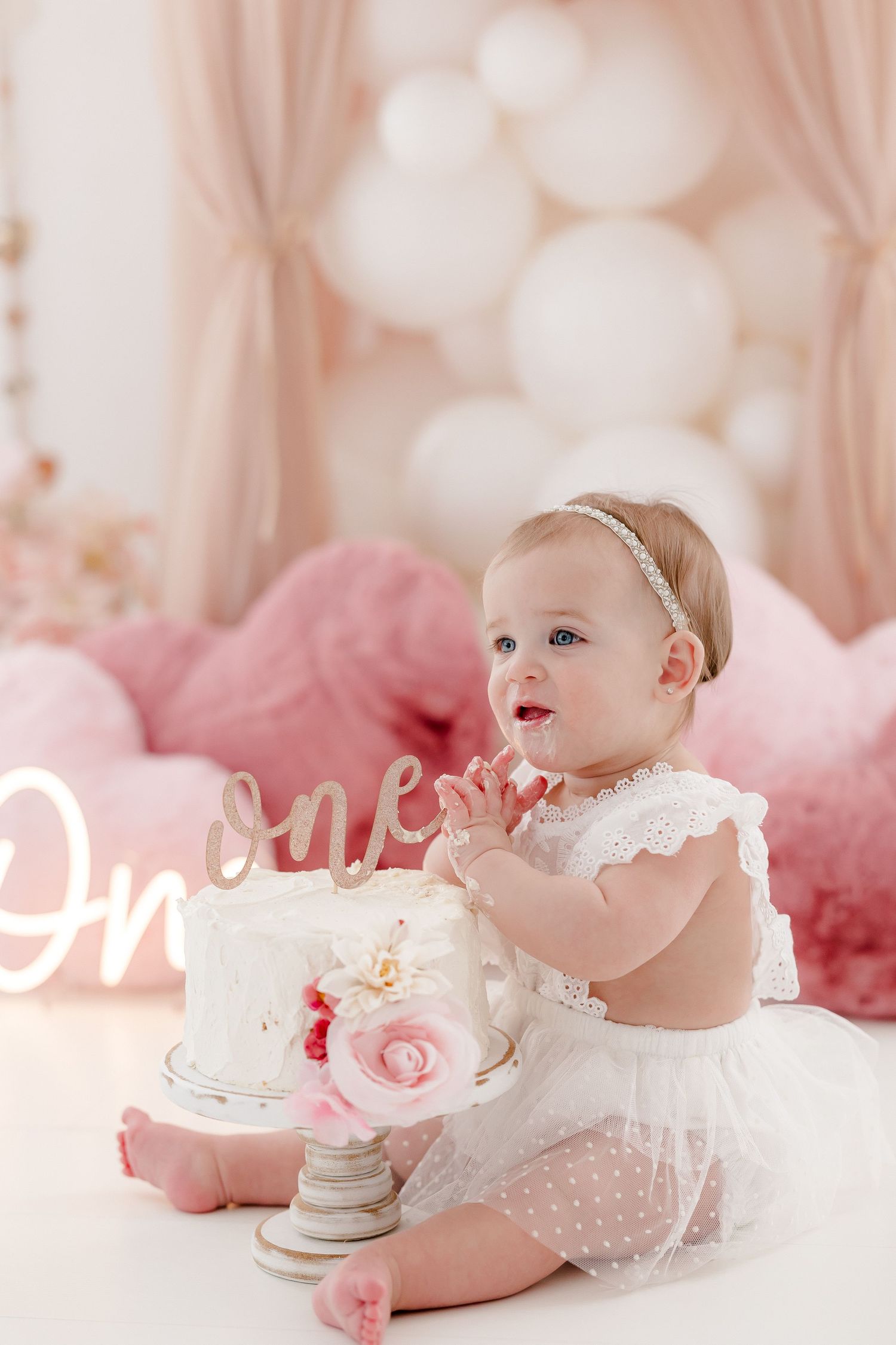 Birthday cake setup with pink tulle decor and glowing 'One' sign.