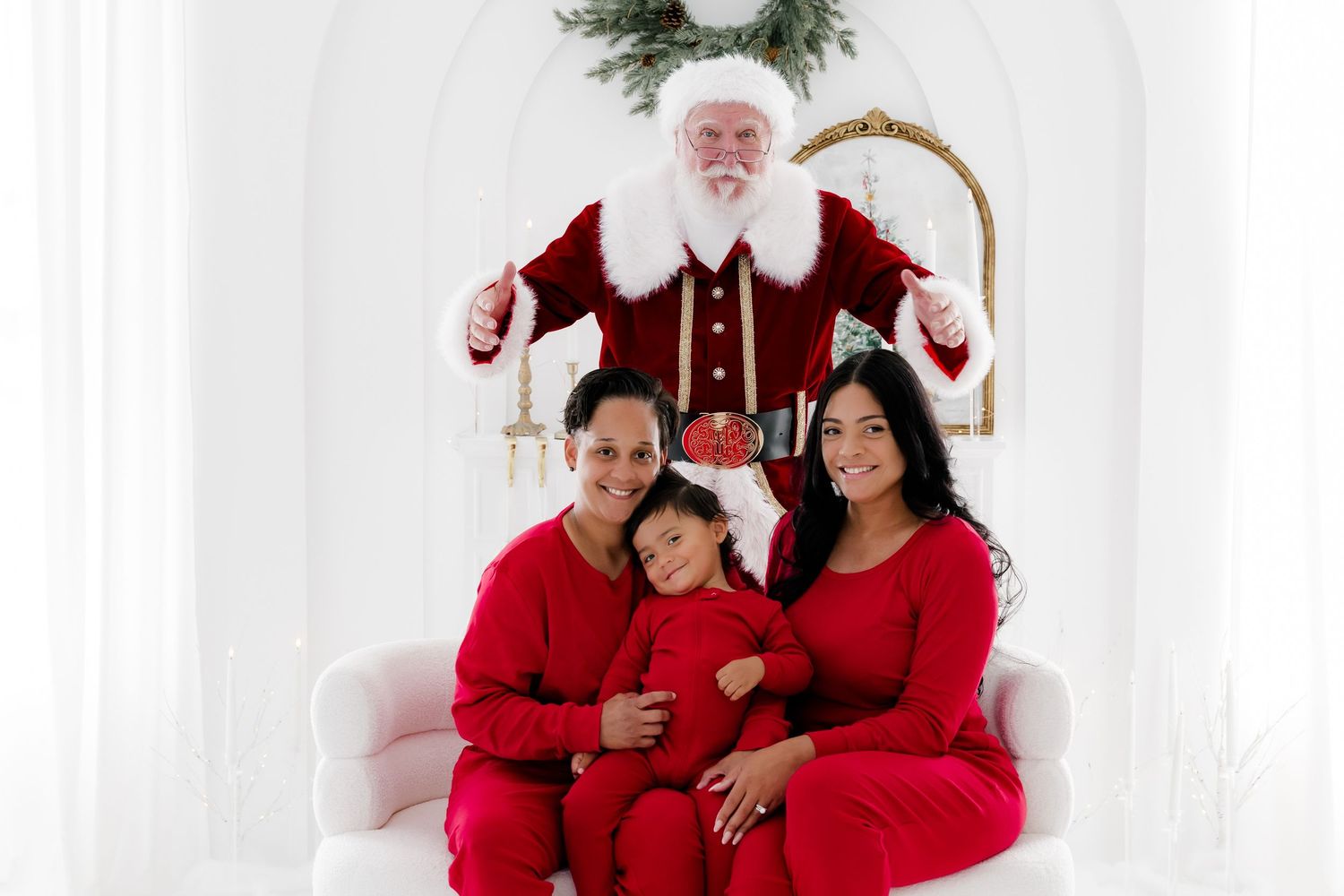 Family in red pajamas poses with Santa Claus in a bright white holiday studio setting.