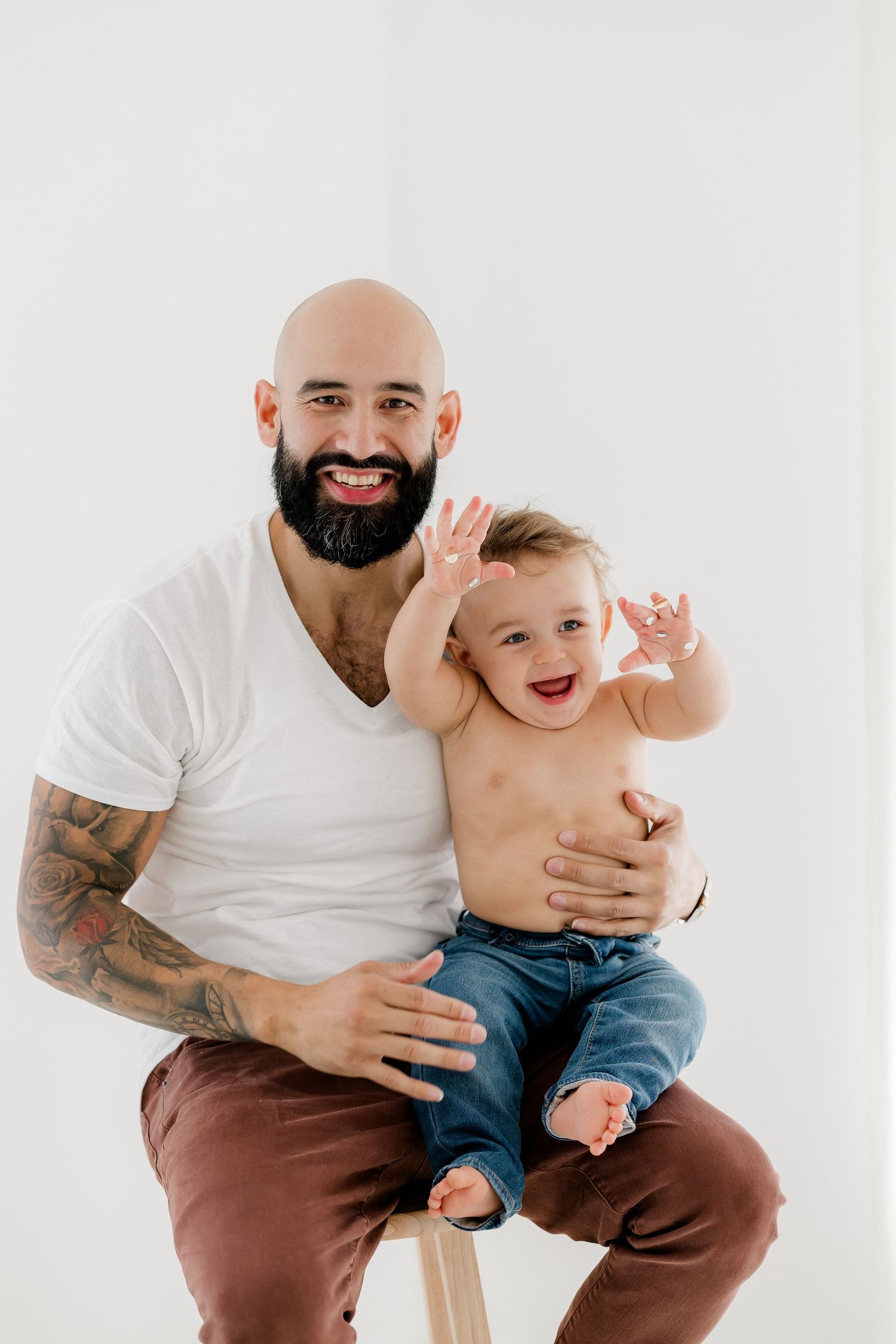A joyful baby in jeans laughs while being held against a white background.