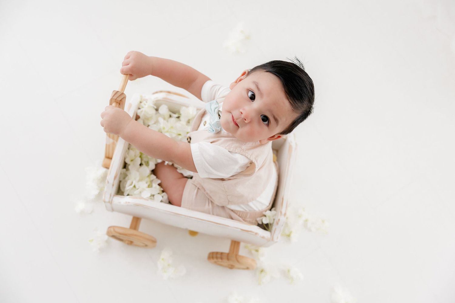 A baby lying on a white blanket surrounded by soft toys and decorative elements.