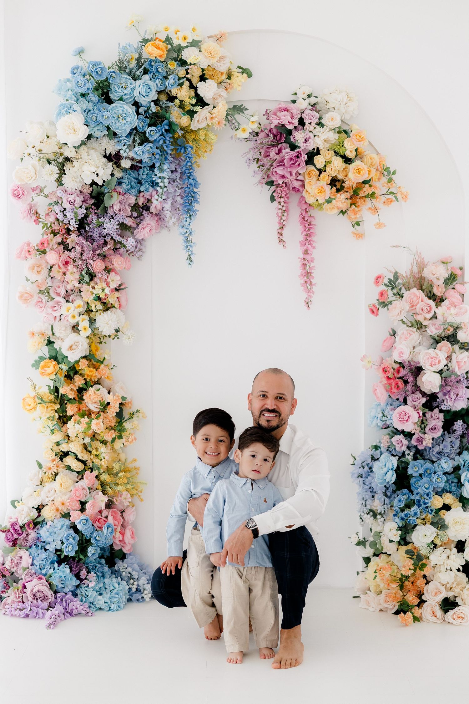 Beautiful floral arch with pastel blue, pink and yellow flowers creates an elegant backdrop for a family portrait.