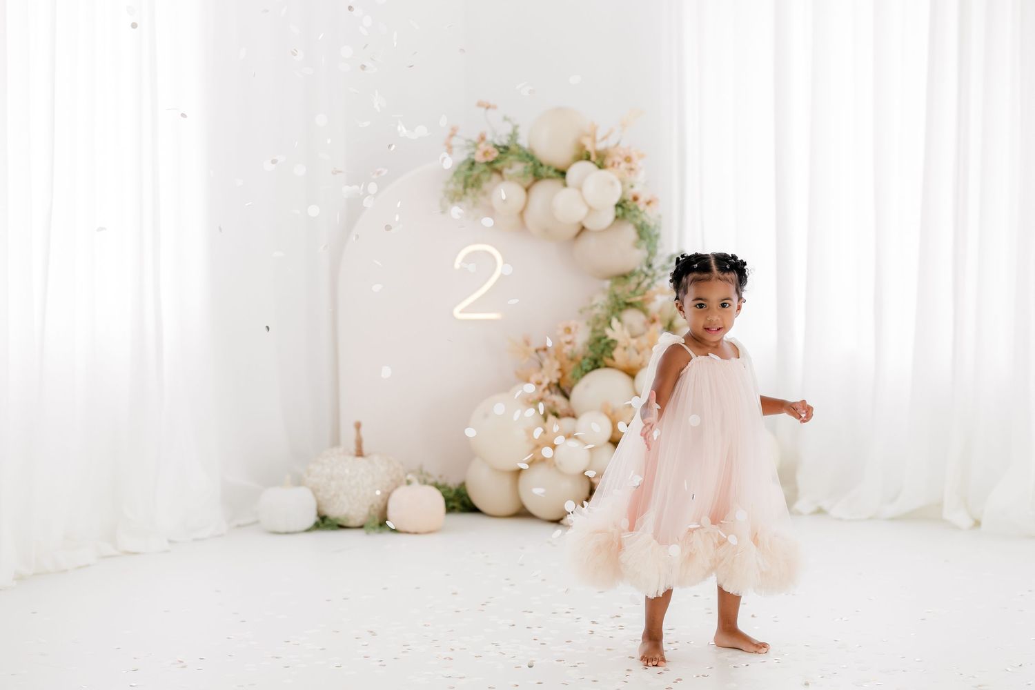 White and pink floral balloon arch decorates an elegant all-white studio space for a special occasion.