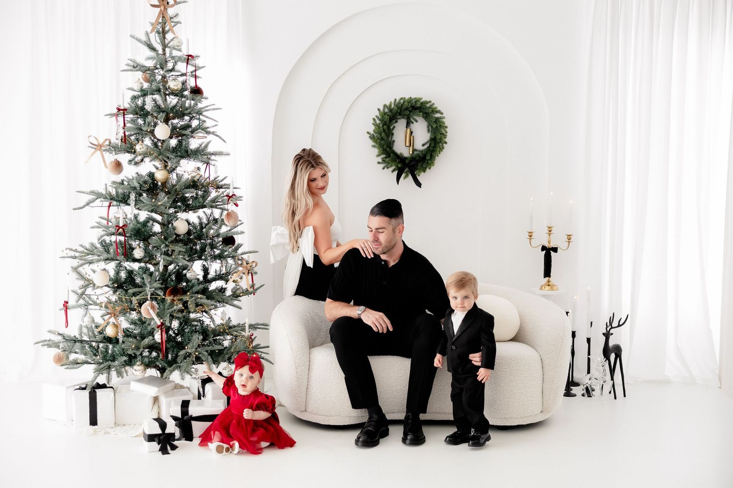 Family Christmas portrait in white room with decorated tree and wreath.