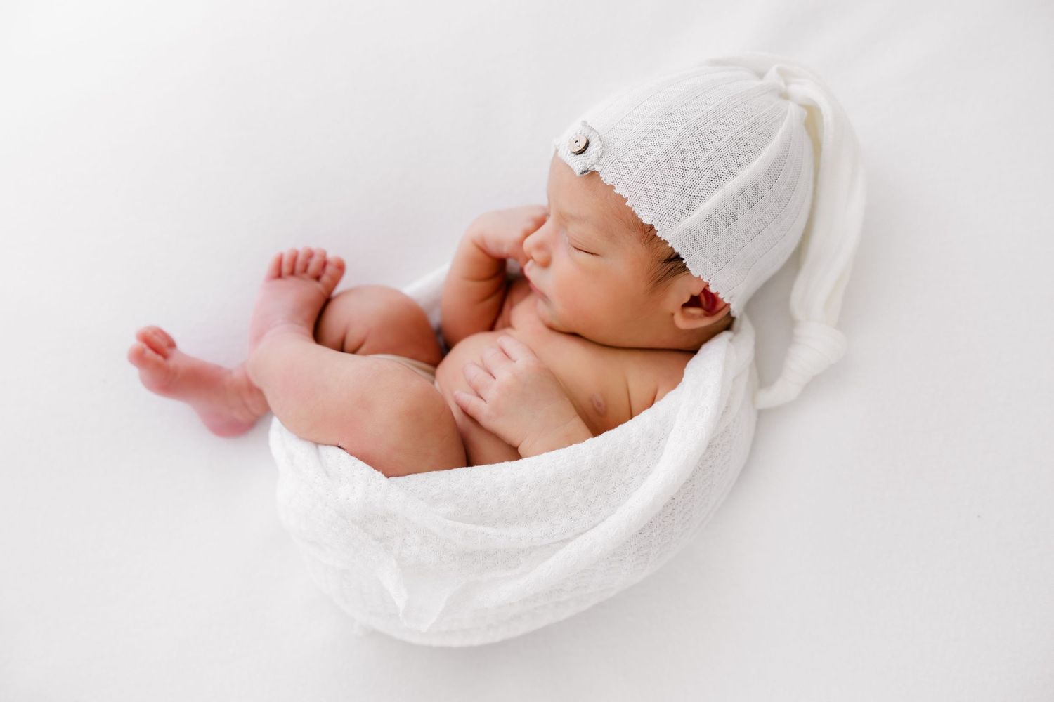 Sleeping newborn wrapped in white blanket on minimalist white background.